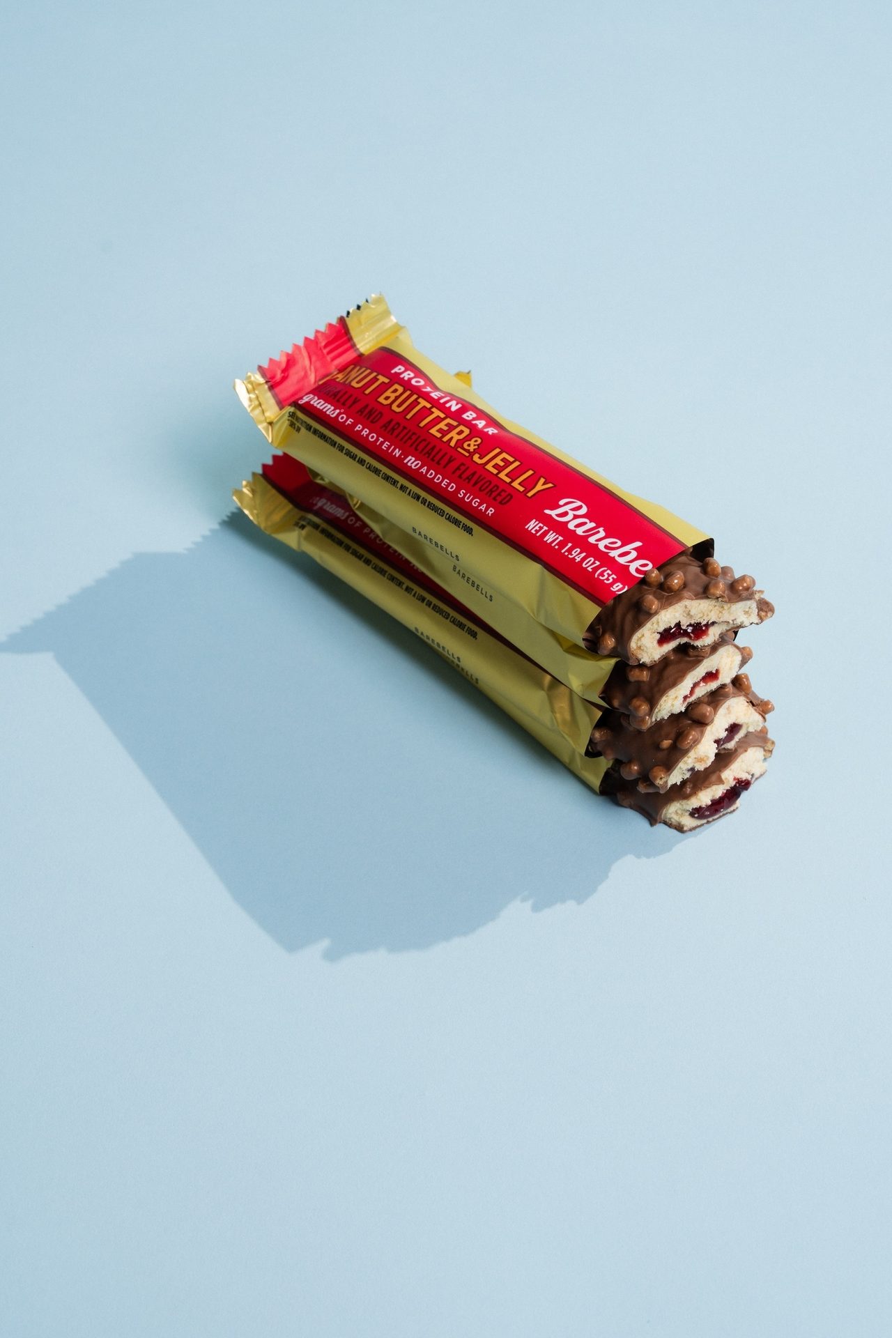 Stacked Barebells Peanut Butter & Jelly protein bars with chocolate coating, showing red filling.