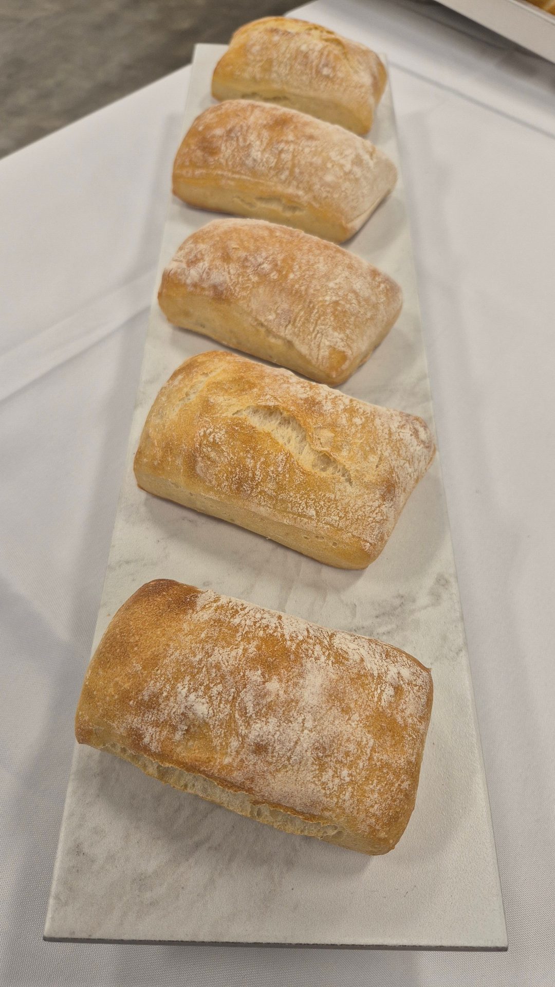 Five golden-brown, flour-dusted bread loaves arranged on a white marble slab.