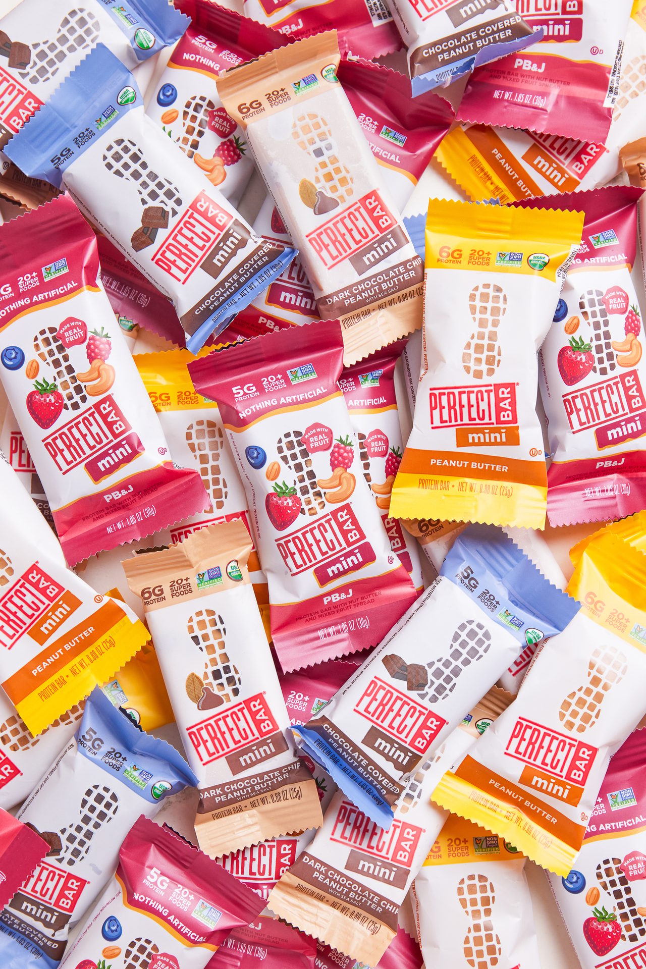 A pile of Perfect Bar mini protein bars in various flavors like Peanut Butter, PB&J, and Chocolate Covered.