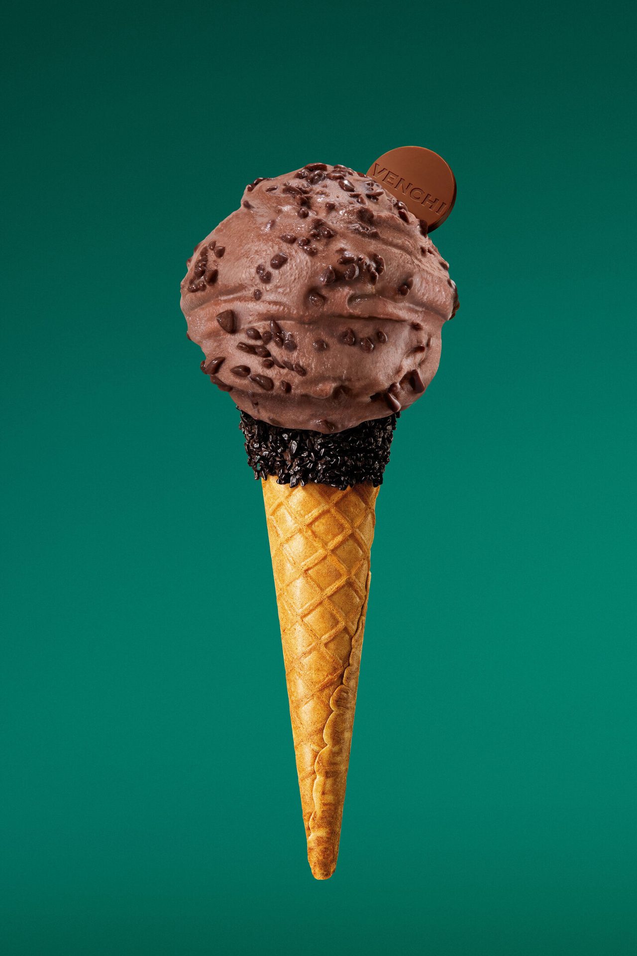 Chocolate ice cream cone with chips, sprinkles, and a Venchi tag on a teal background.