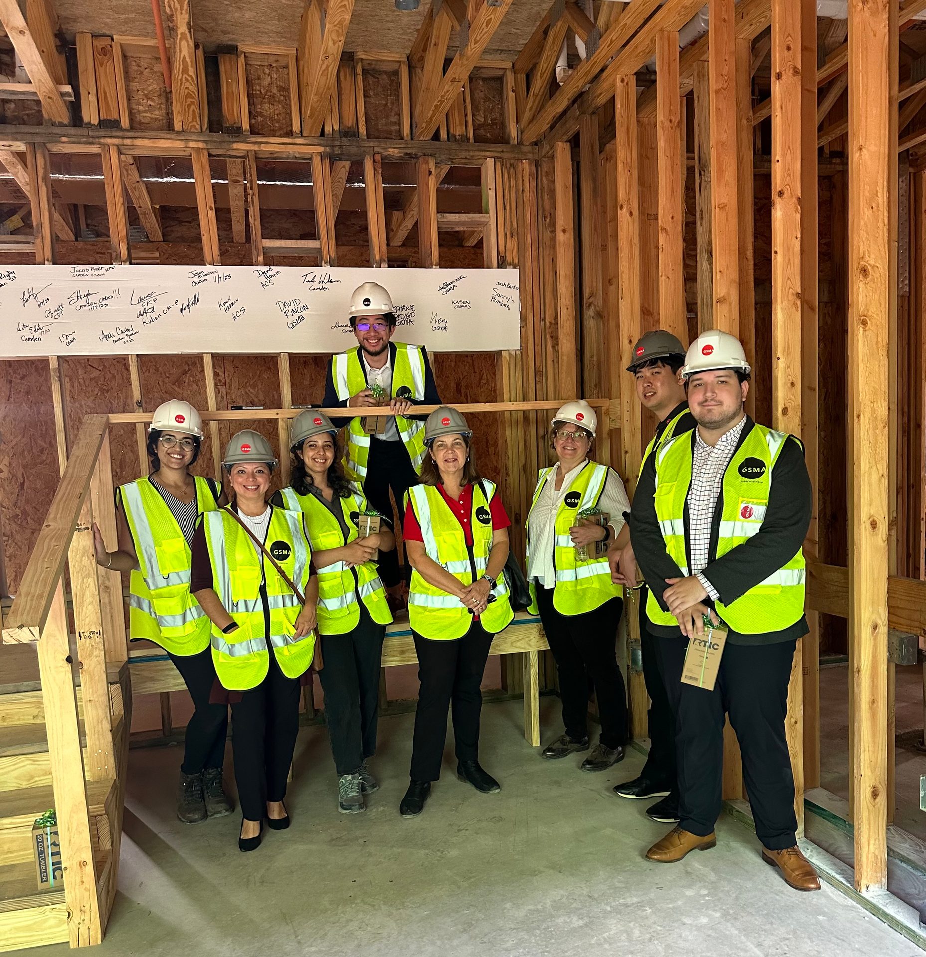 A group of people in safety vests and hard hats on a construction site, some holding plants.