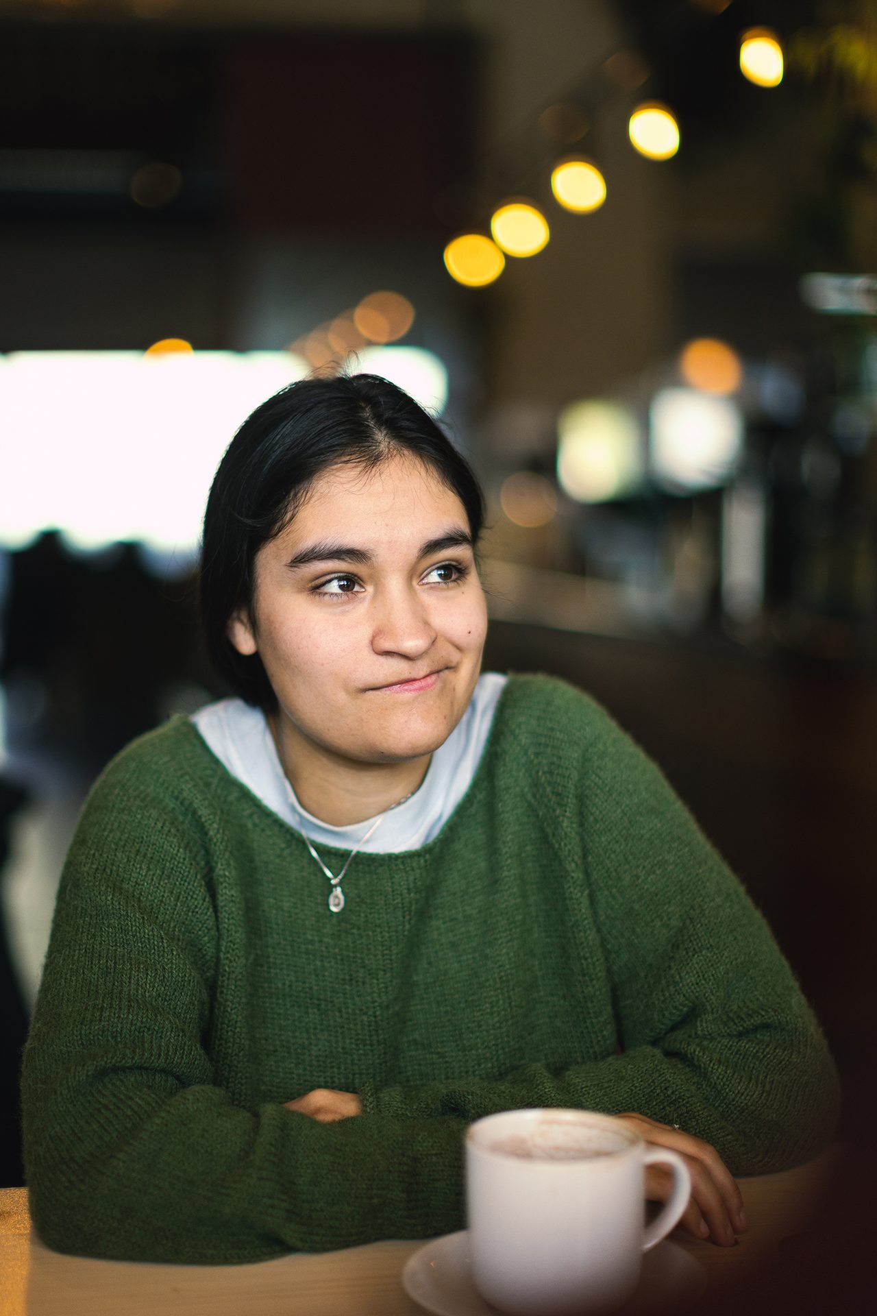 Portrett av en ung kvinne med m&#xF8;rkt h&#xE5;r som sitter med en kaffekopp ved siden av. Hun ser tankefull ut.