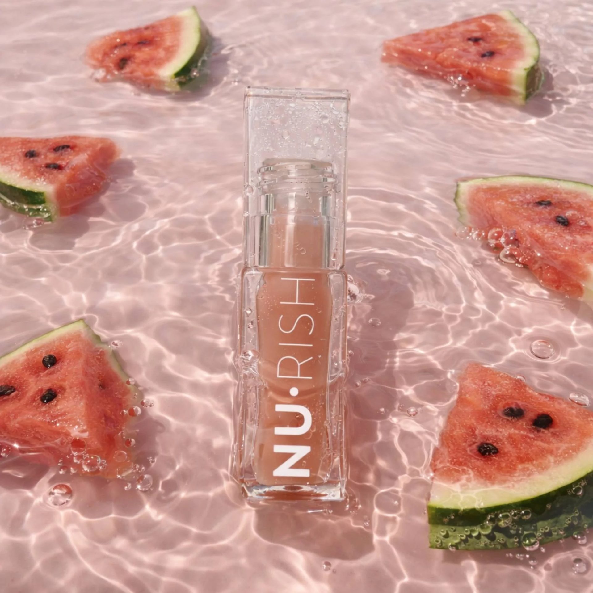 NU.RISH lip product in clear packaging floating in pink water with watermelon slices and bubbles.