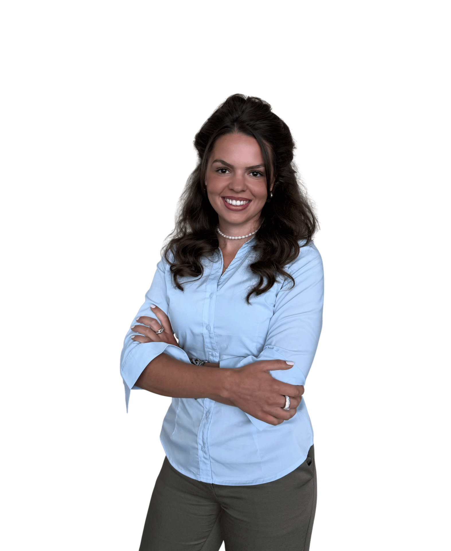 Smiling woman in light blue shirt, olive pants, and pearl necklace, with arms crossed.