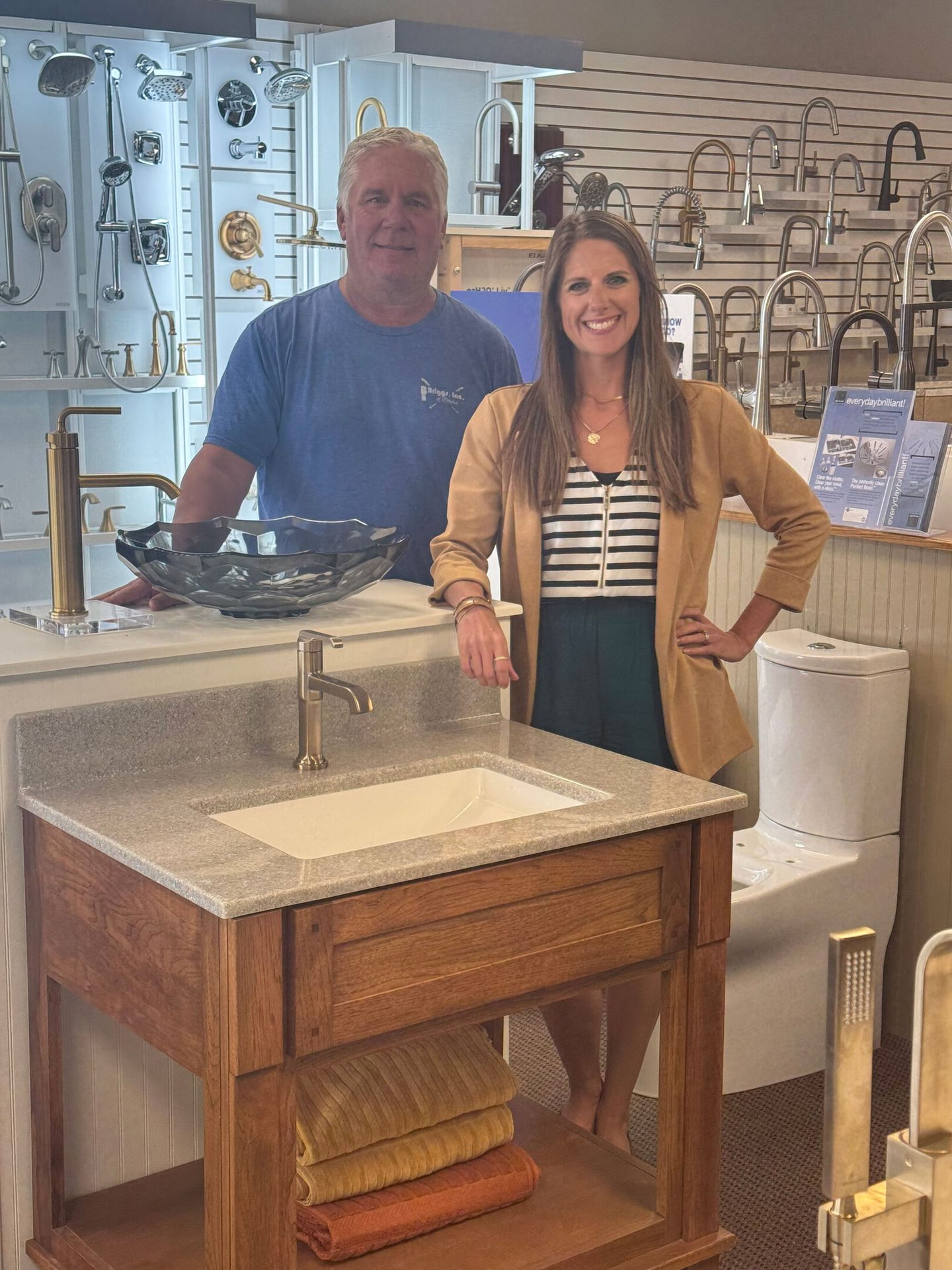 Smiling man and woman in a plumbing showroom with faucets, showers, and a vanity.