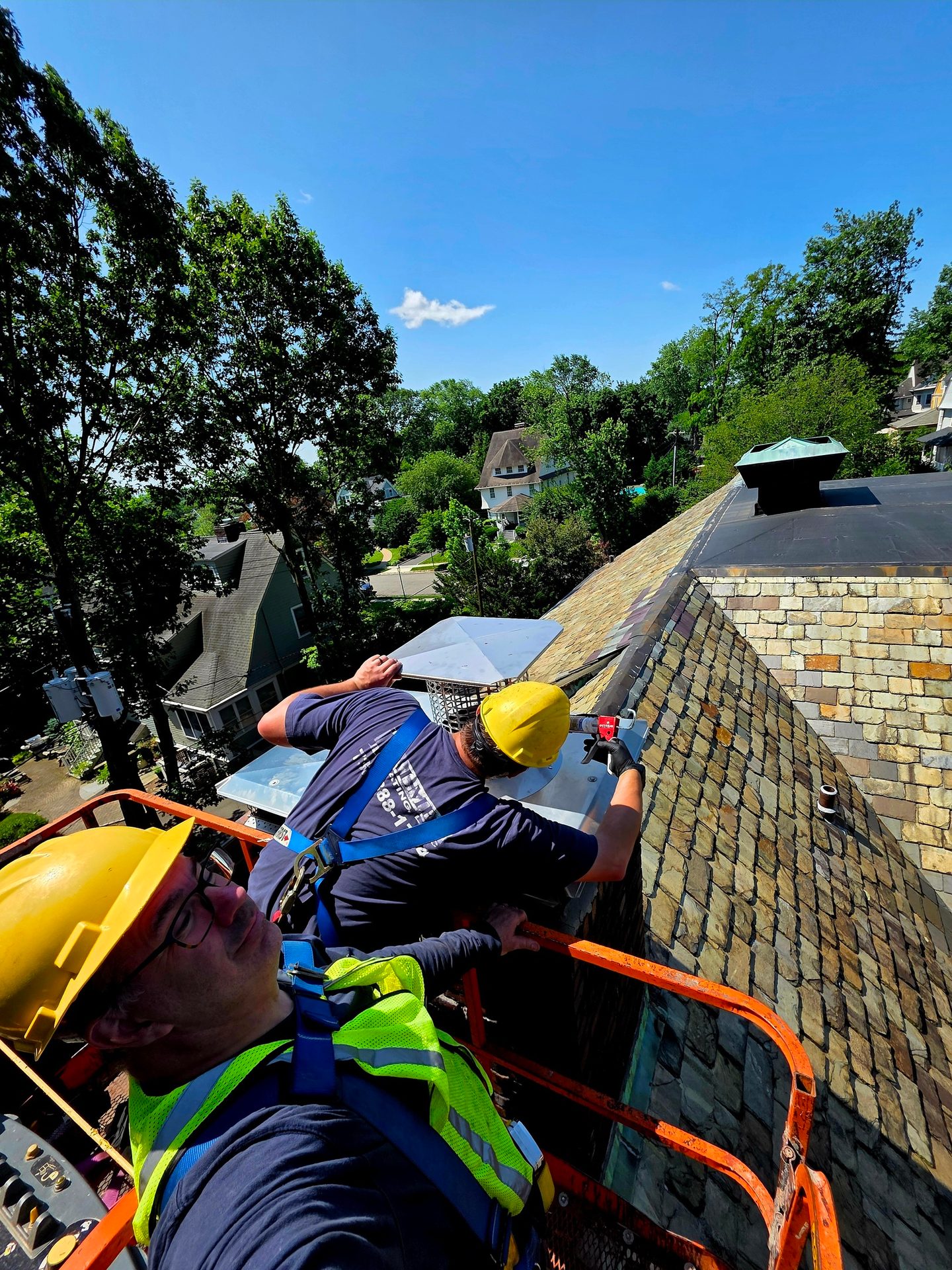 Two workers in hard hats on a lift, installing or repairing a stone roof.