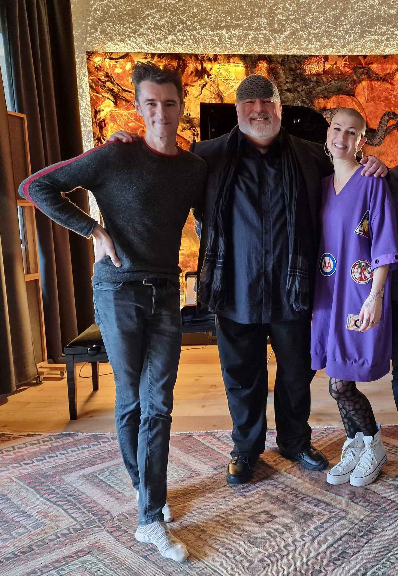 Two smiling men and one woman pose for a photo indoors.