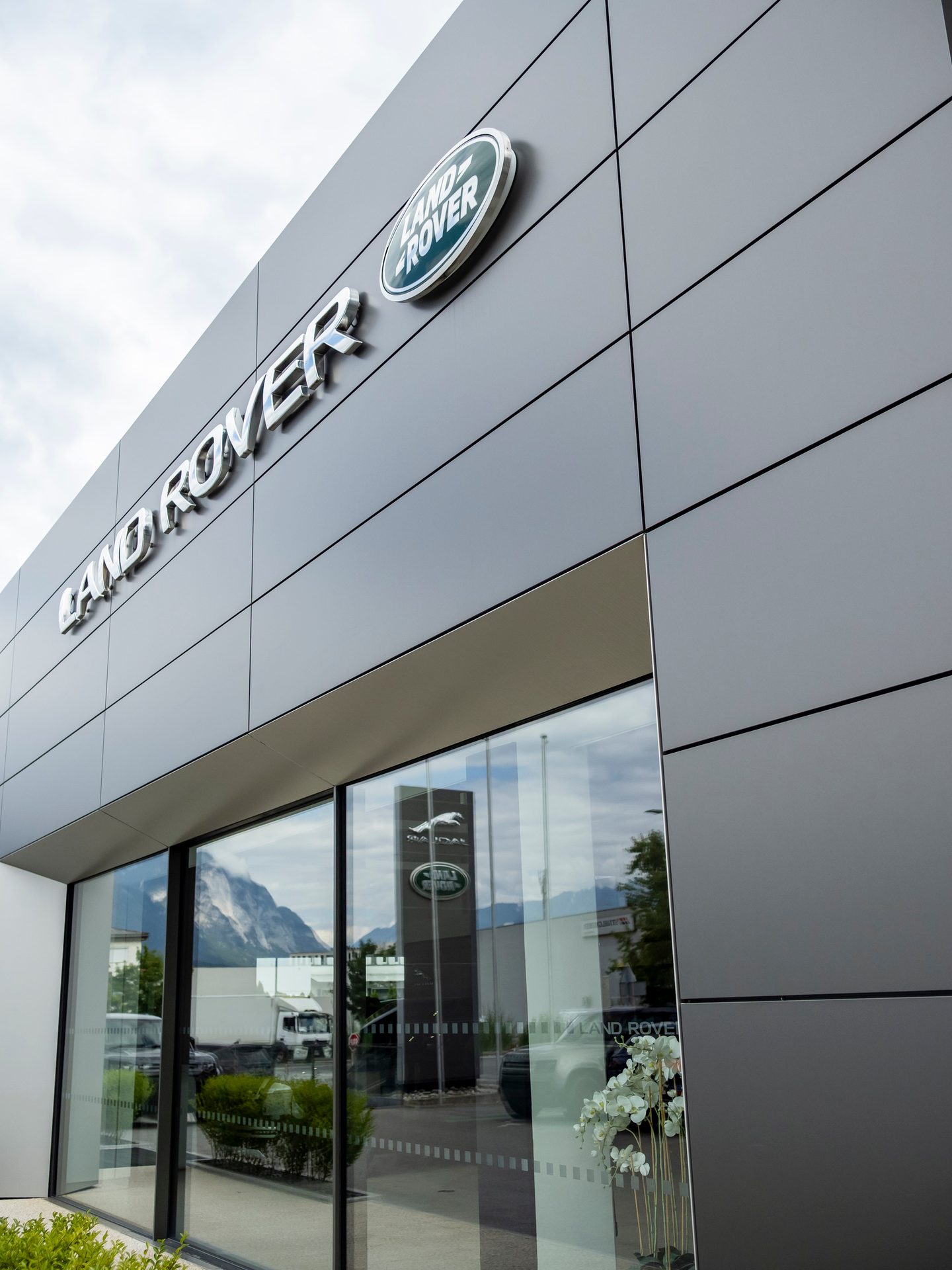 Land Rover dealership exterior with its logo and reflections of mountains and vehicles.