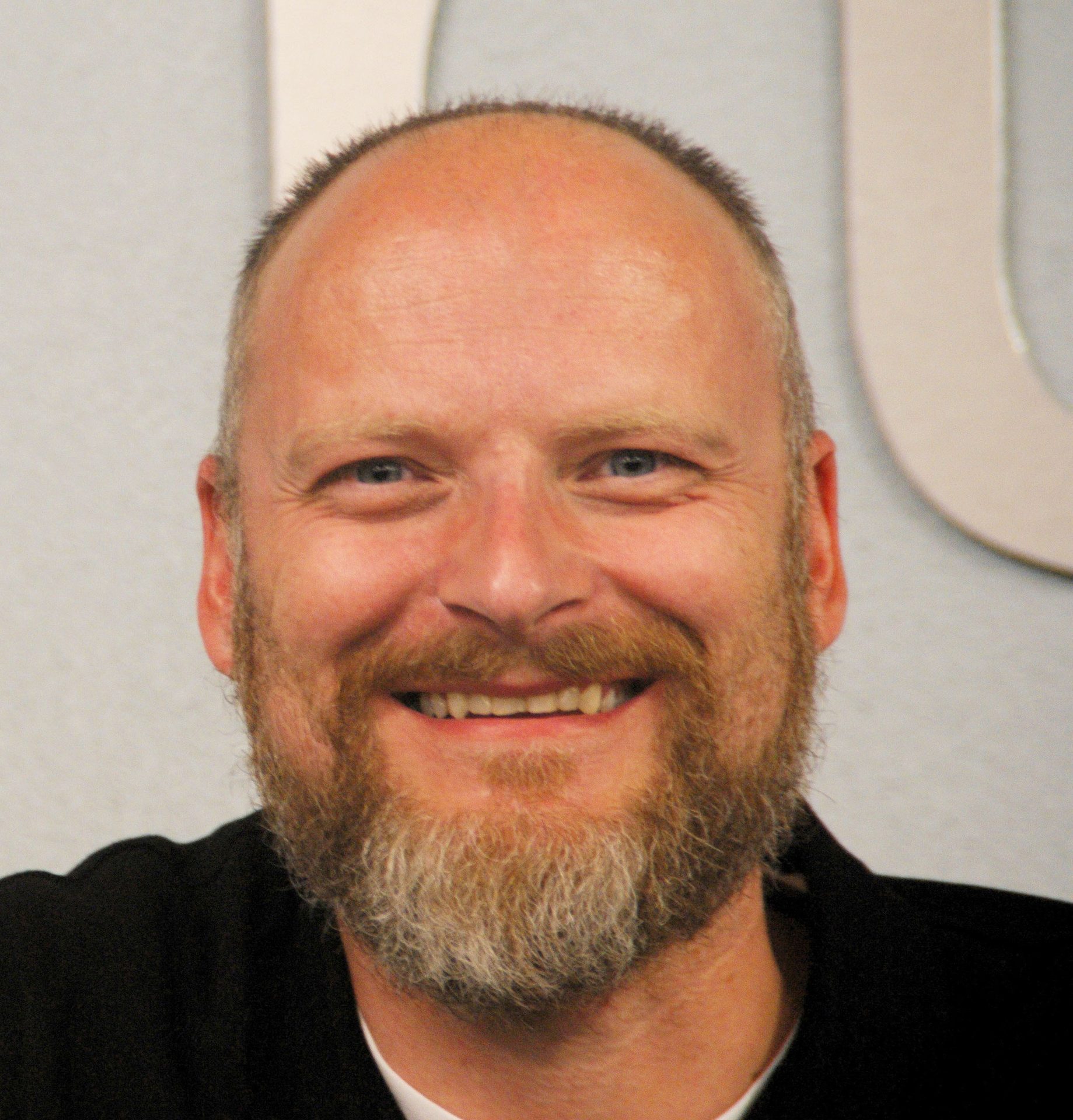 Close-up of a smiling man with a beard and receding hairline looking directly at the camera.