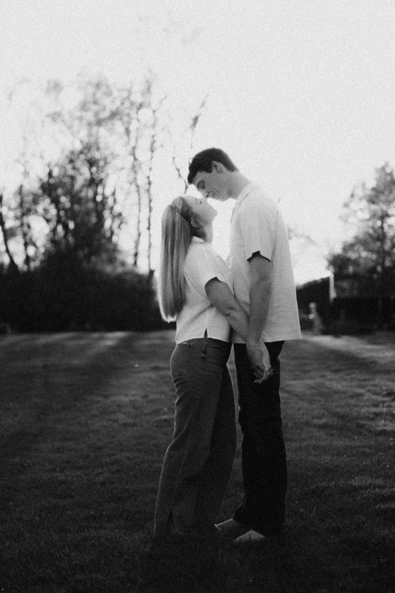 Backlit B&W photo of a couple holding hands, gazing lovingly at each other in a field.