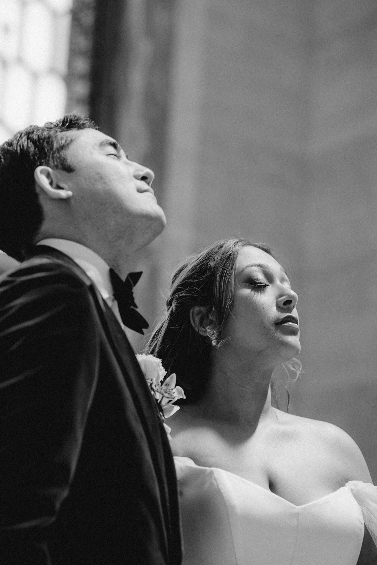 Black and white image of a bride and groom looking up with serene, closed eyes.