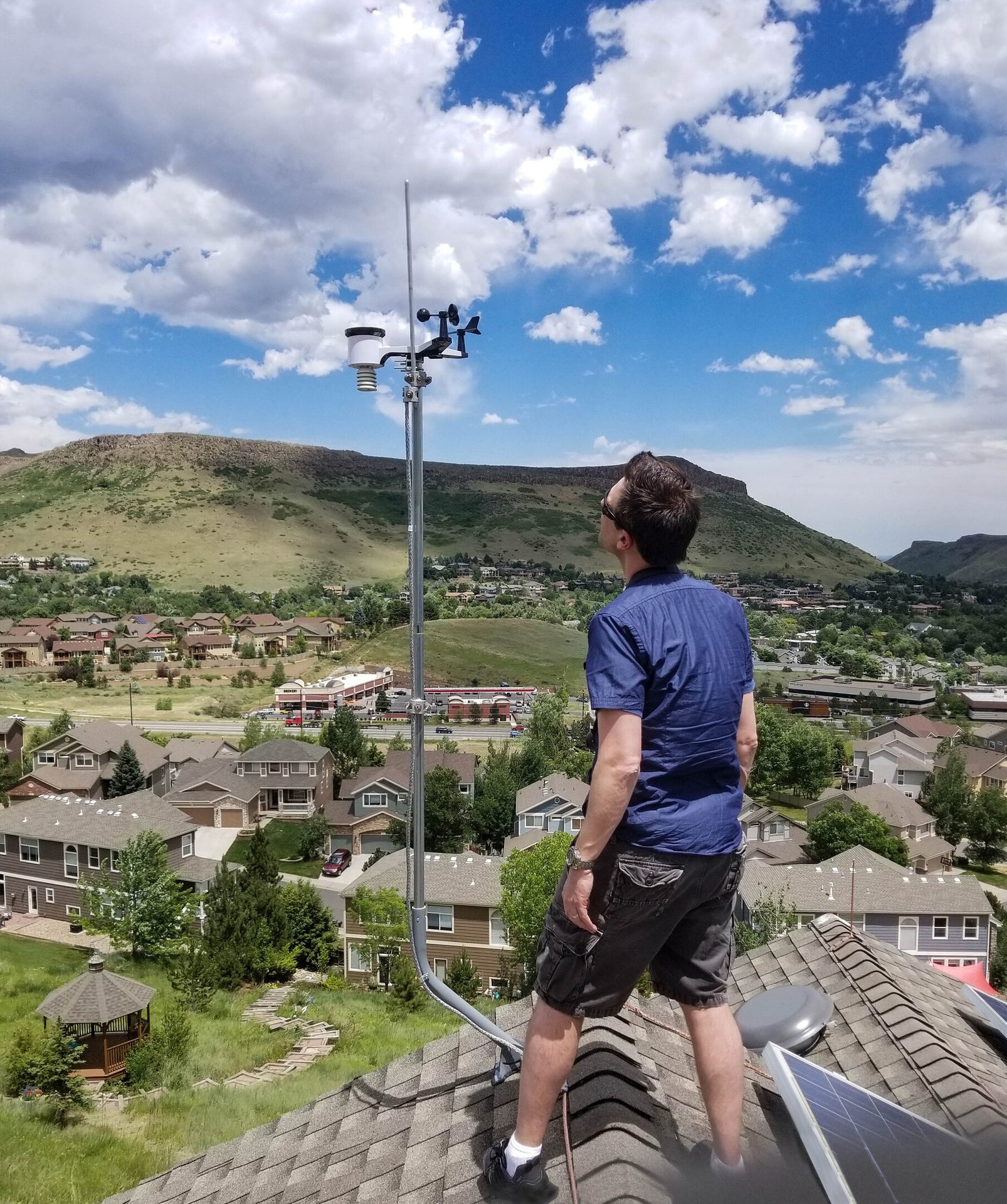 Man on a roof with a weather station, overlooking a town and mountains.