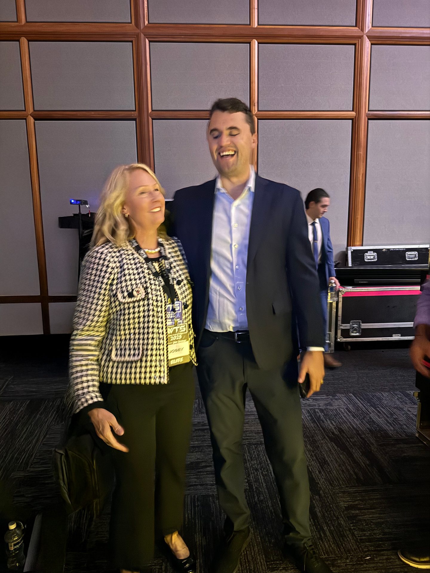 A blonde woman and a man in a suit laughing together at an event.