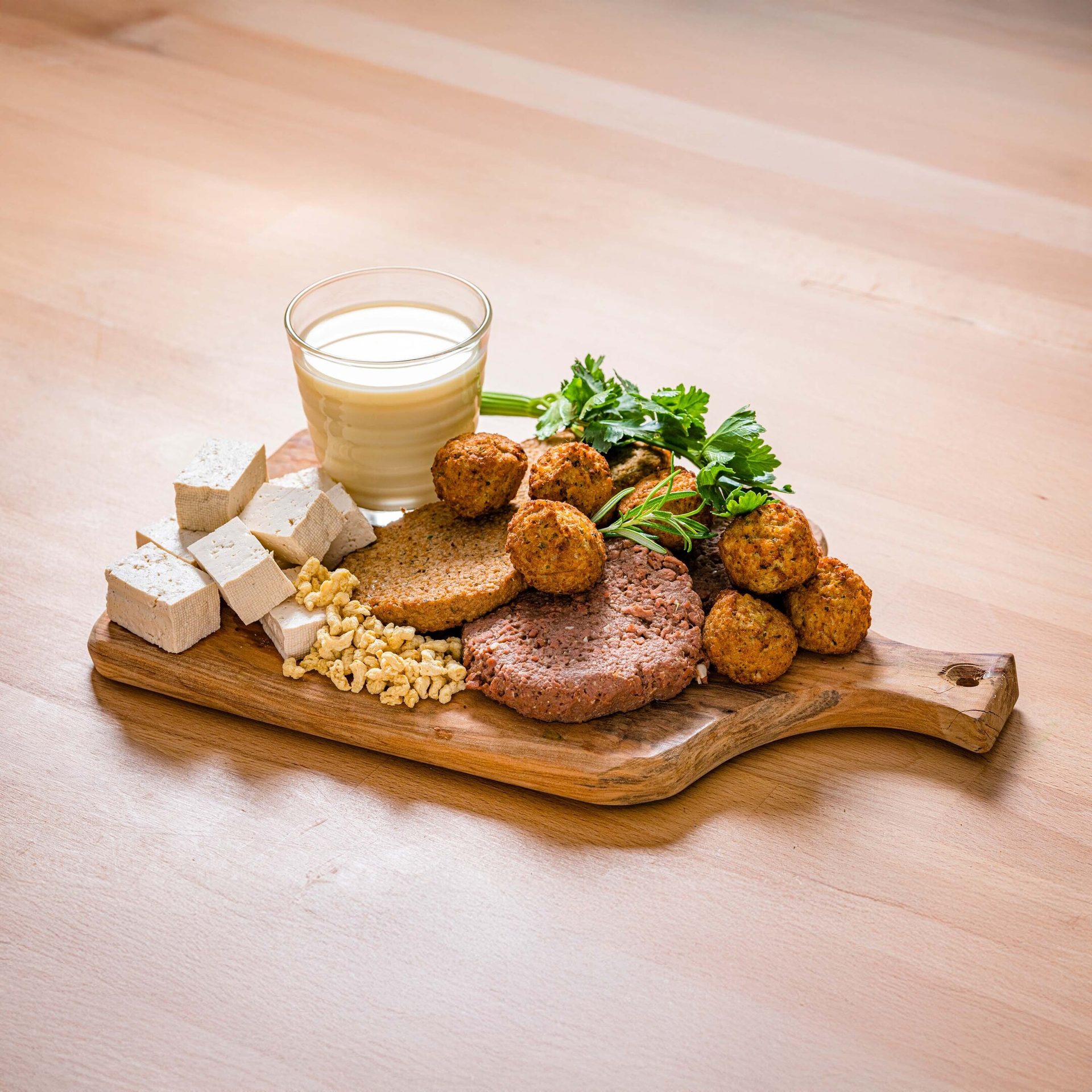 A wooden board displaying various plant-based proteins: tofu cubes, patties, falafel, soy chunks, and milk.