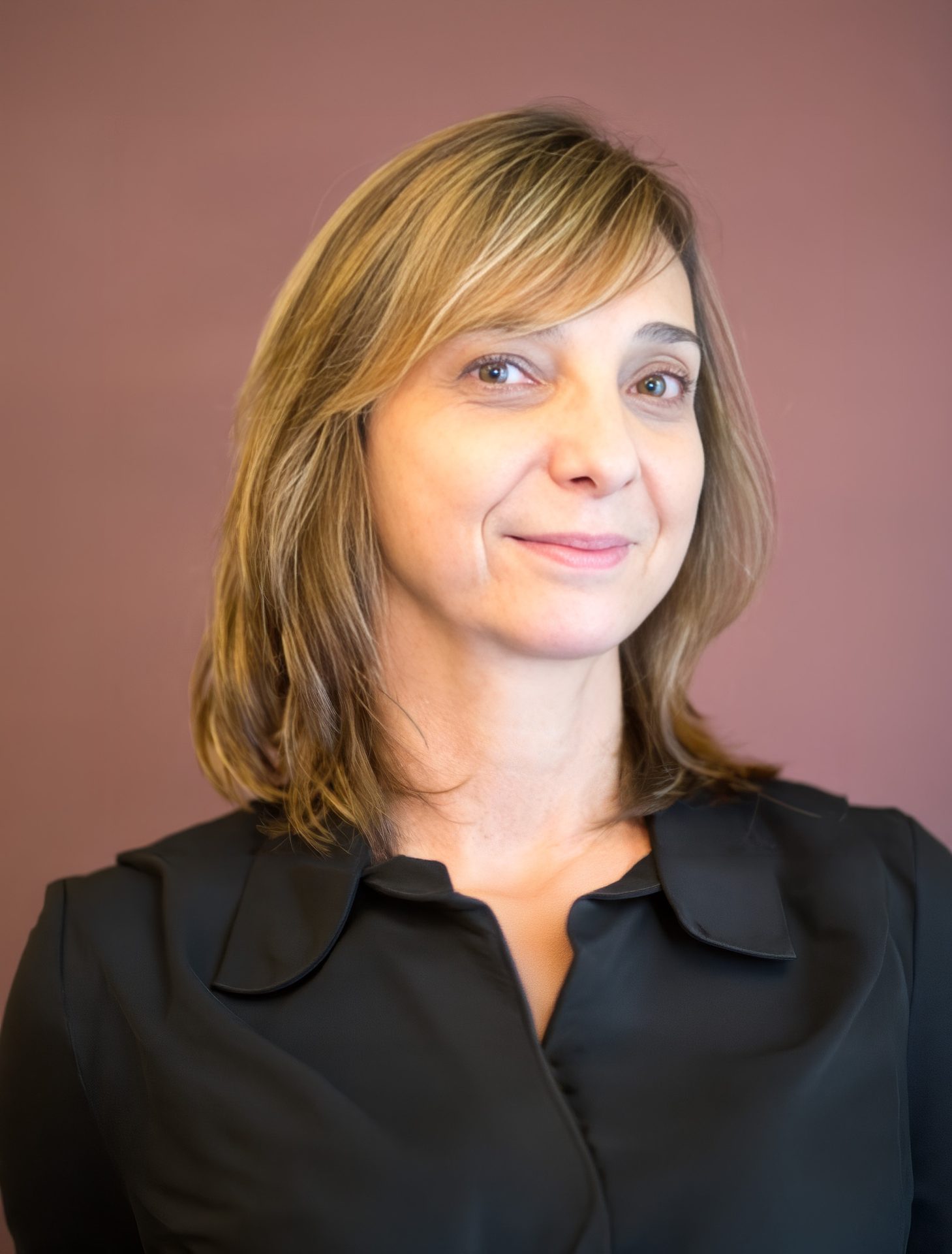 A smiling woman with shoulder-length blonde hair and a black shirt against a plain background.