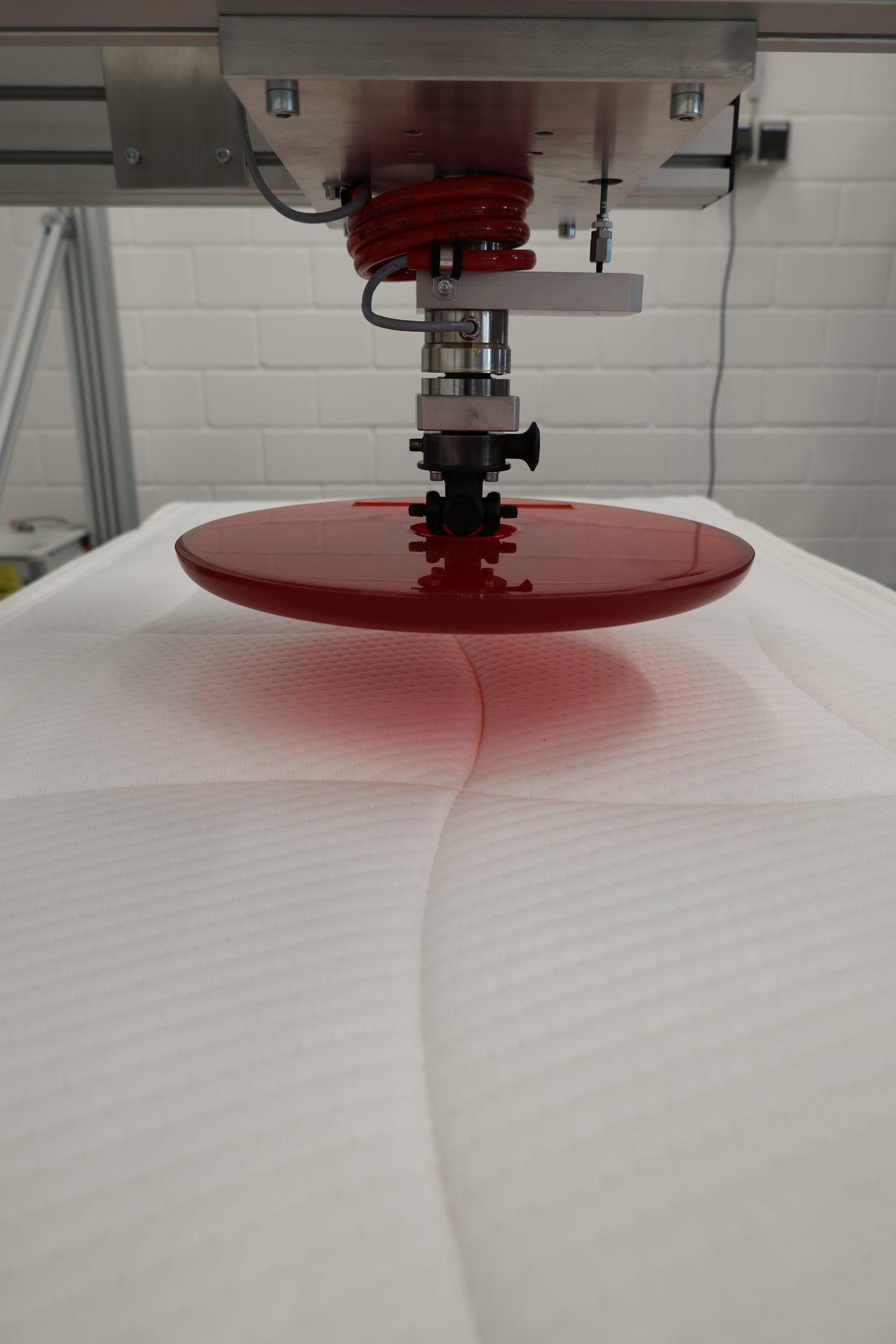 A red circular plate from a testing machine pressing into a white mattress.