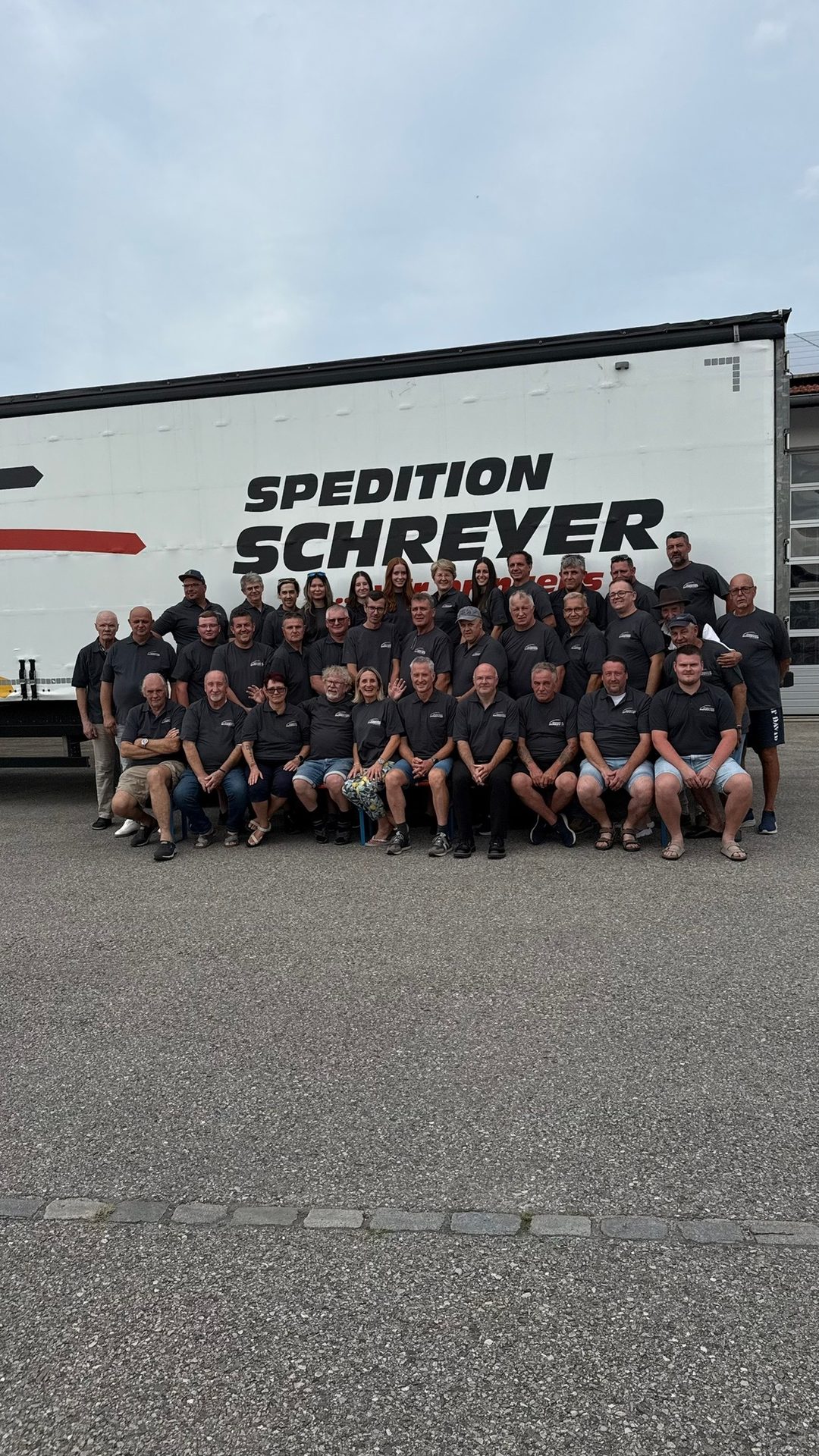 A large group of Spedition Schreyer employees poses in gray shirts in front of a company truck.