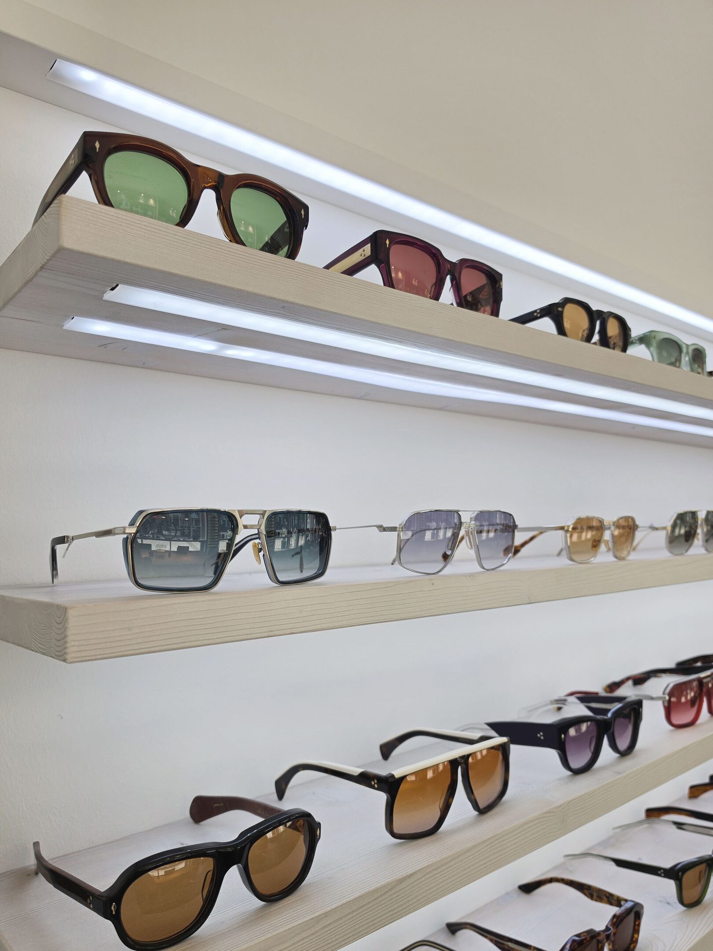 Display of various sunglasses on lighted wooden shelves in a retail store, showcasing different styles.