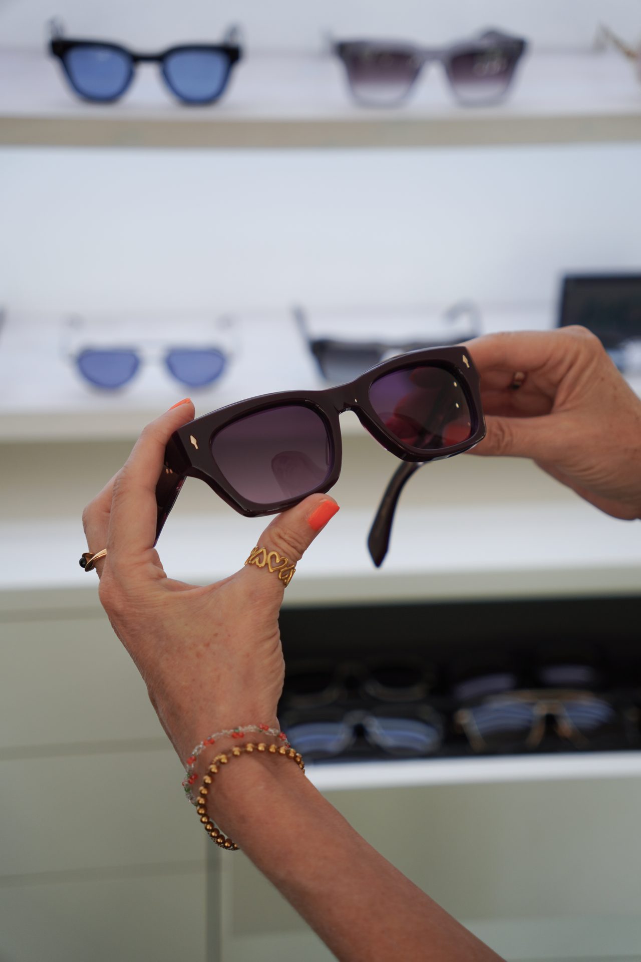 Hands holding dark sunglasses, with other pairs blurred in the background.