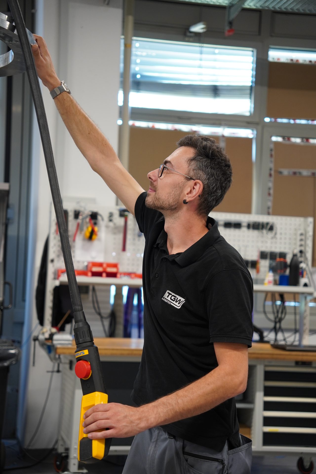 Man in a workshop adjusting equipment with a control panel and reaching up.