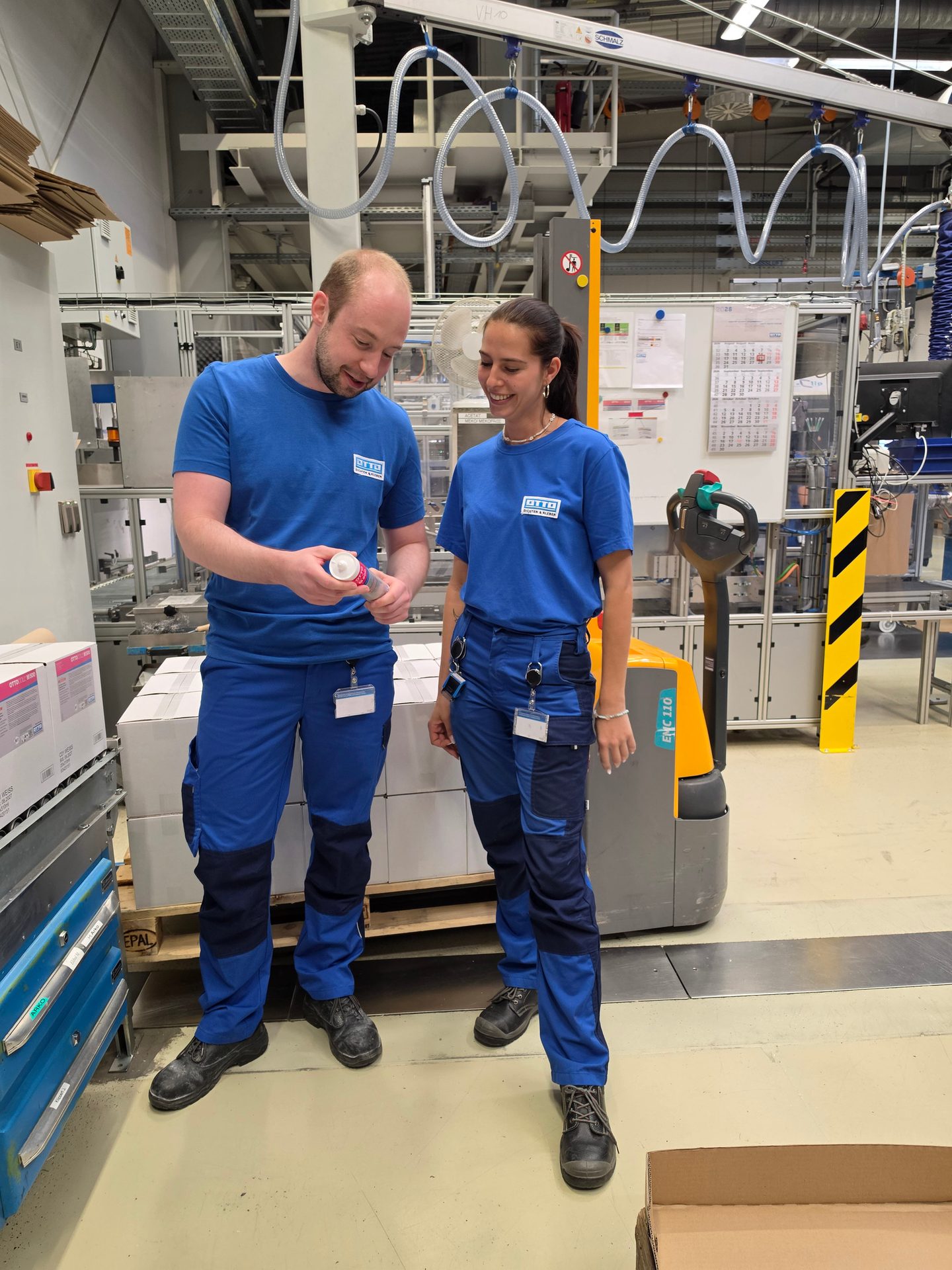 Two factory workers in blue uniforms inspecting a product tube in an industrial setting.