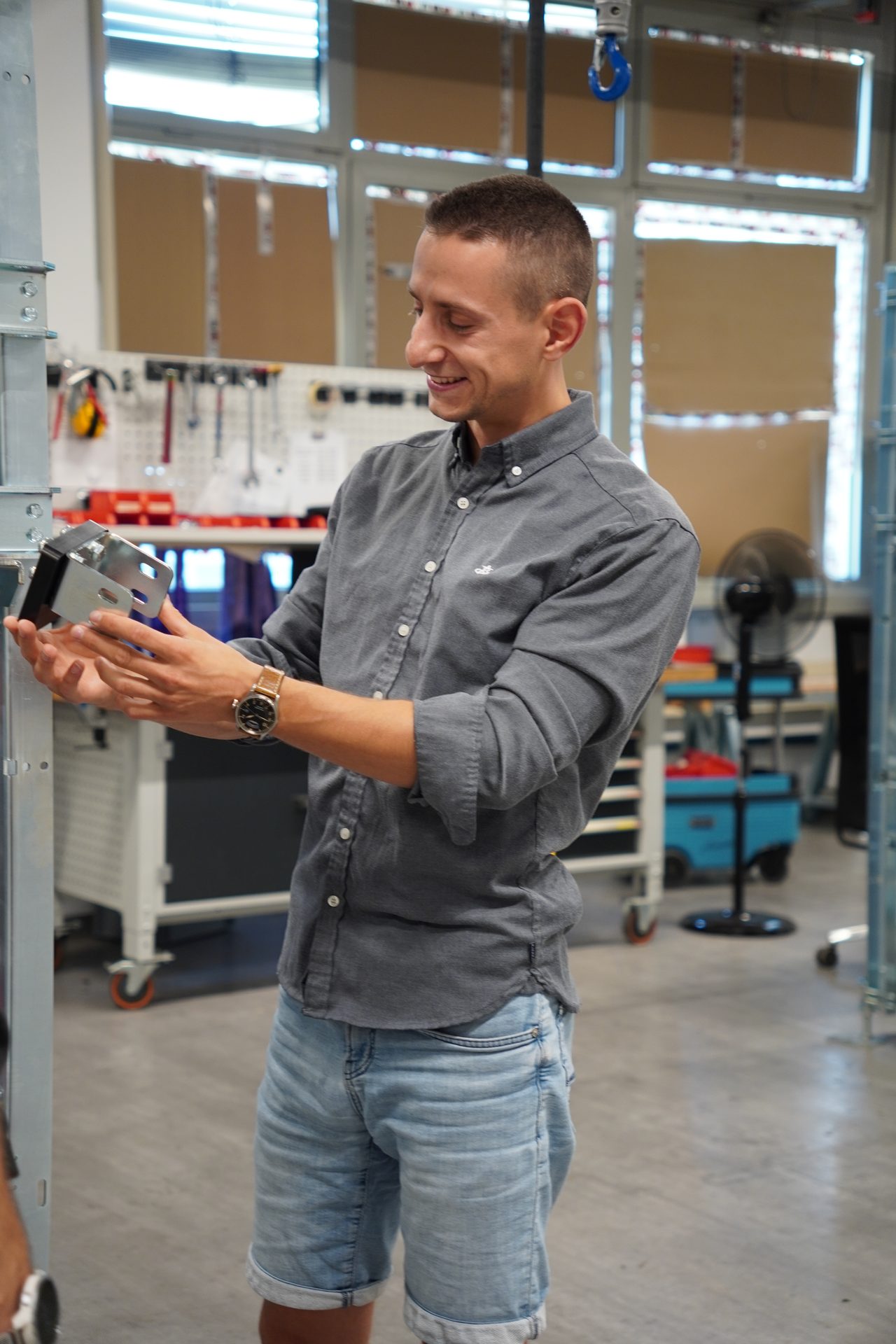 Young man smiling while examining a metal component in a workshop.