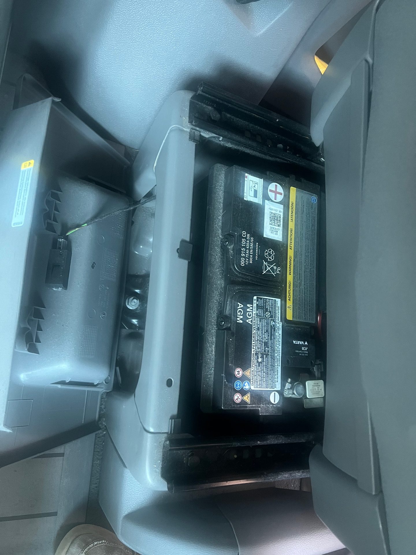 A VARTA AGM car battery with a Volkswagen part number, located inside a vehicle compartment.