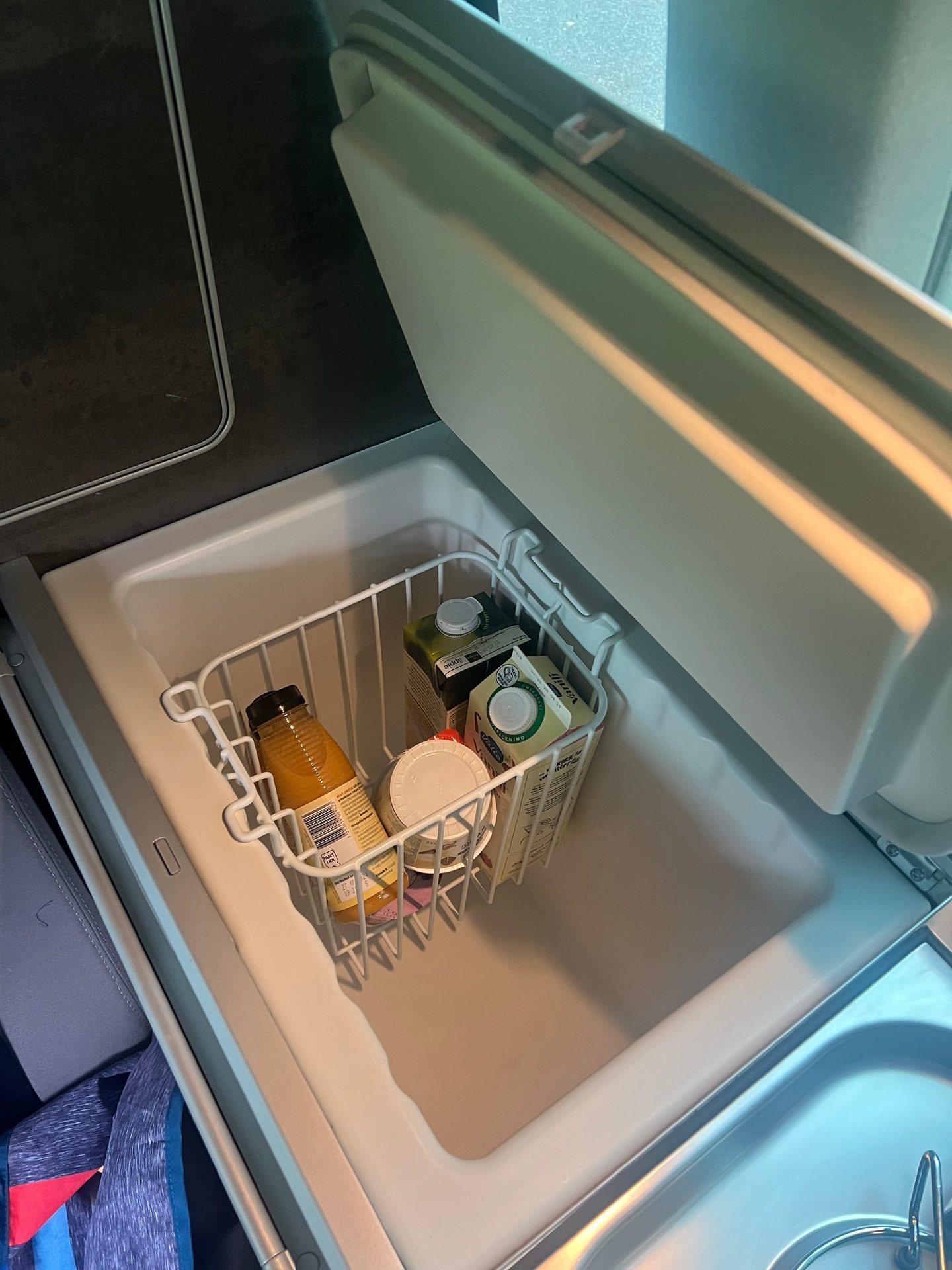 An open top-loading cooler in a camper, containing drinks in a white wire basket.