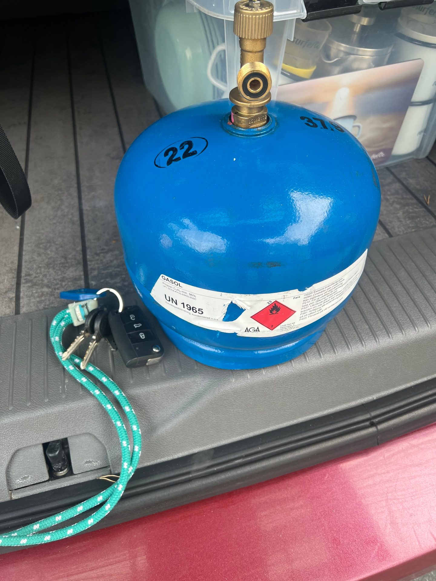 Blue GASOL gas cylinder with valve and car keys in a car trunk.
