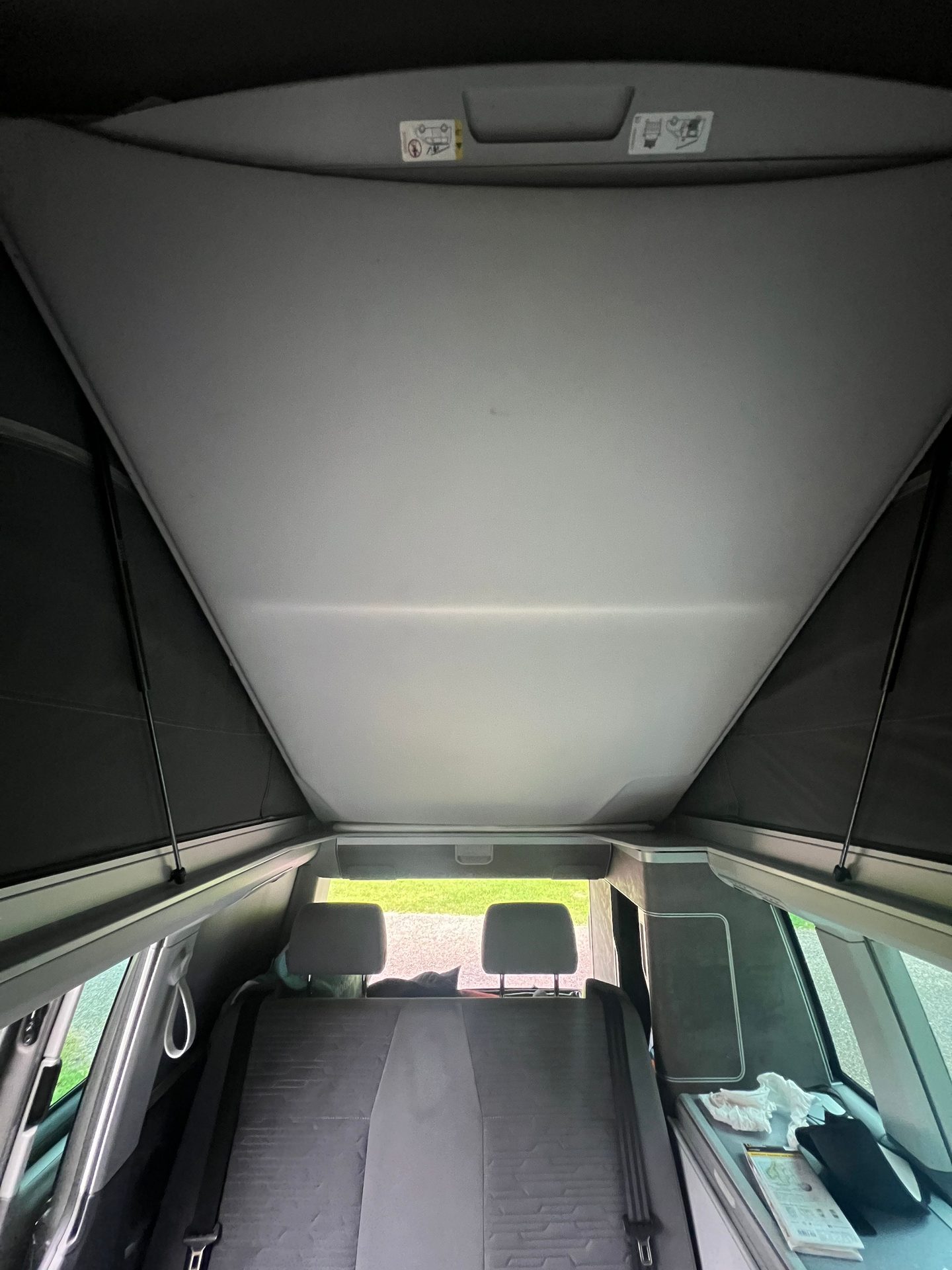 Camper van interior with pop-up roof open, showing rear seats.