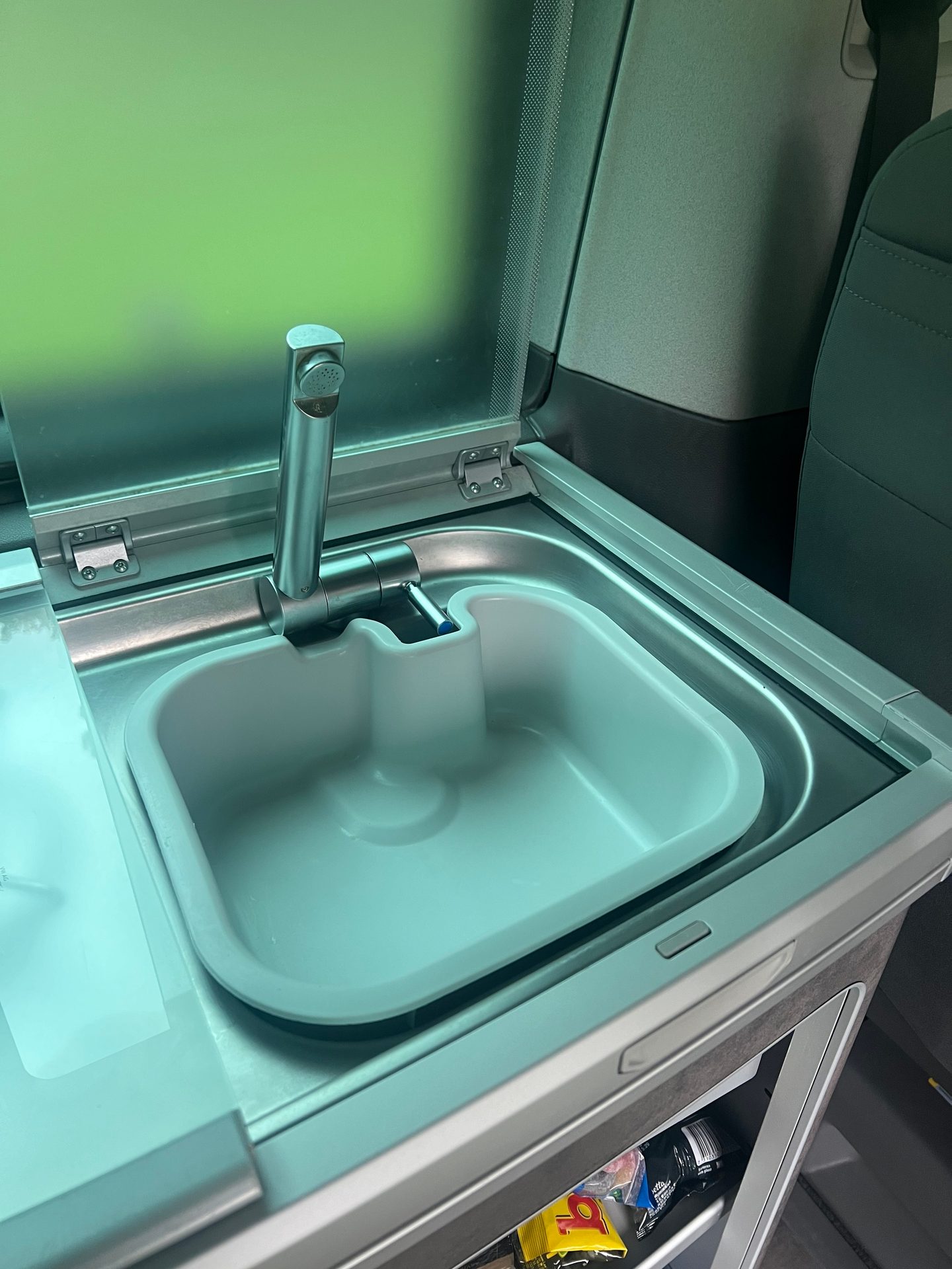 Compact sink and faucet in a camper van, with an open translucent green cover.
