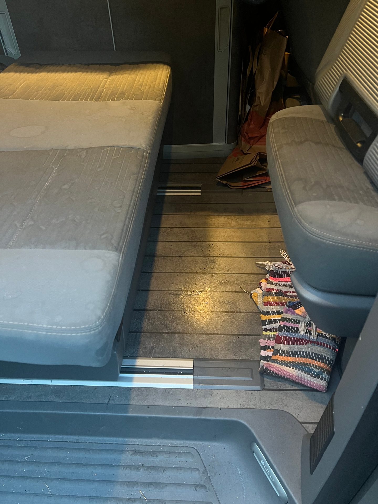 Van interior with bed, seat, wood floor, and colorful rug.