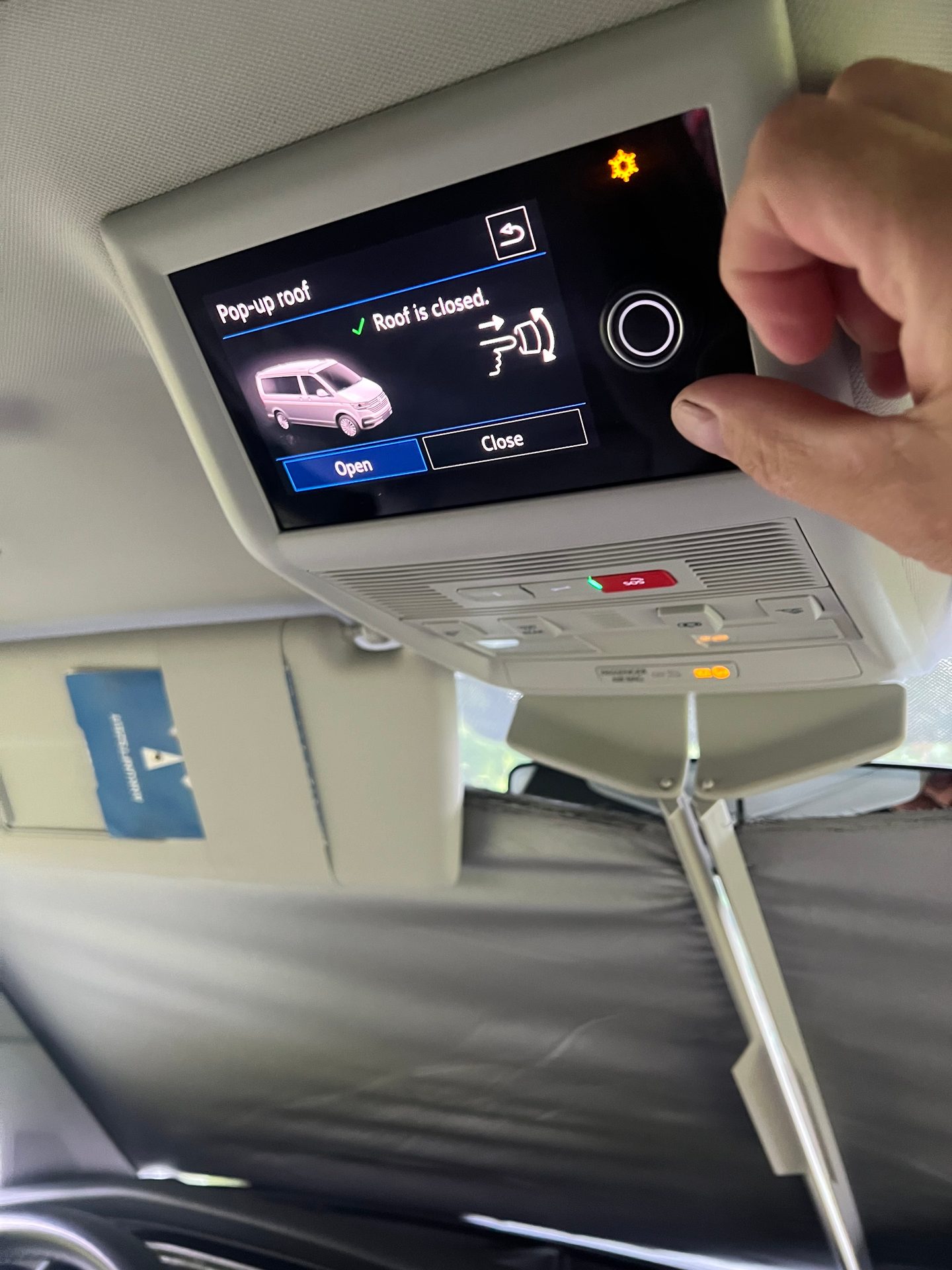 Hand turns dial on car's overhead screen showing "Pop-up roof" control and "Roof is closed."
