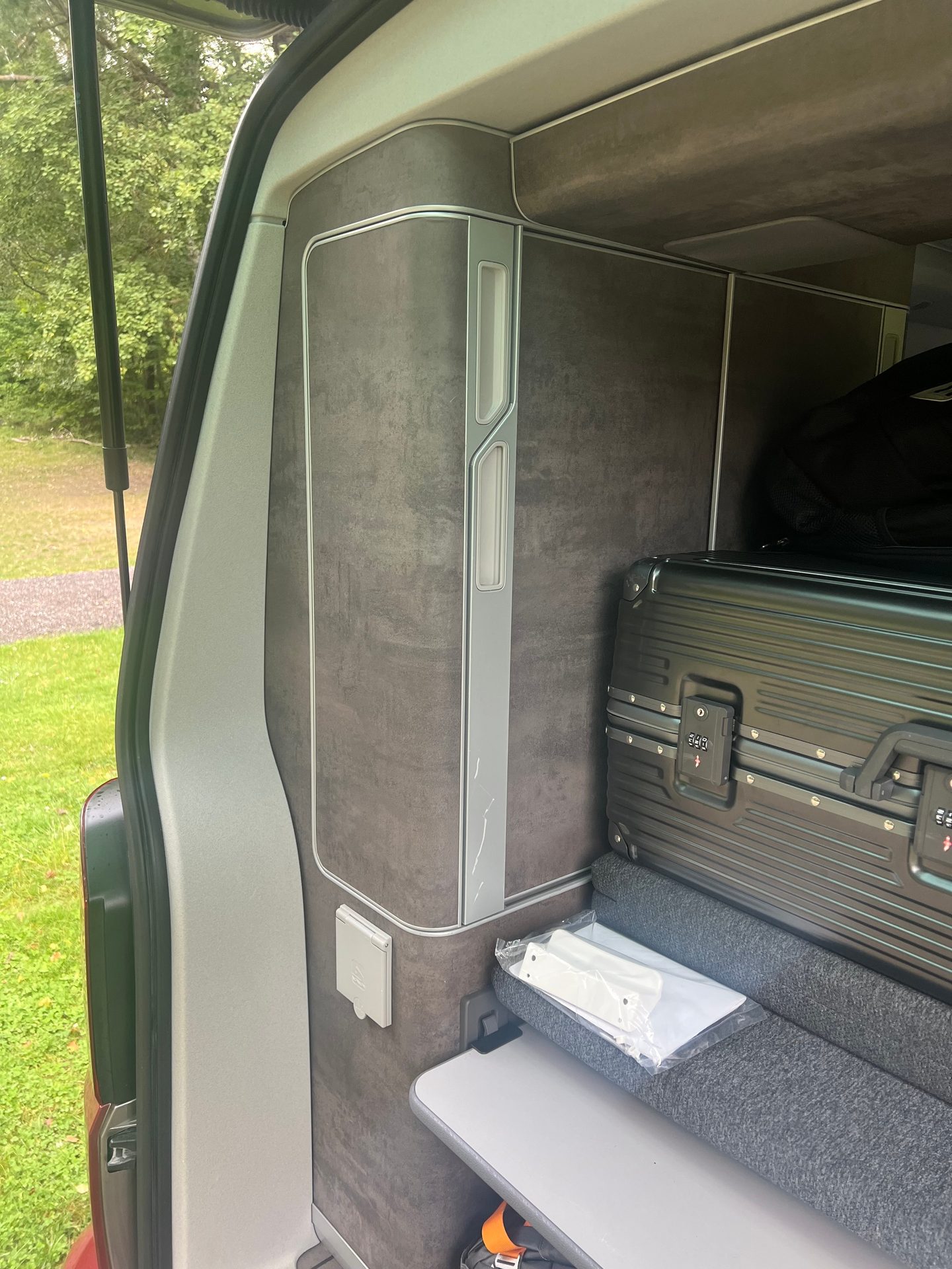 Camper van interior: dark cabinets, black suitcase, fold-down table, and power outlet.