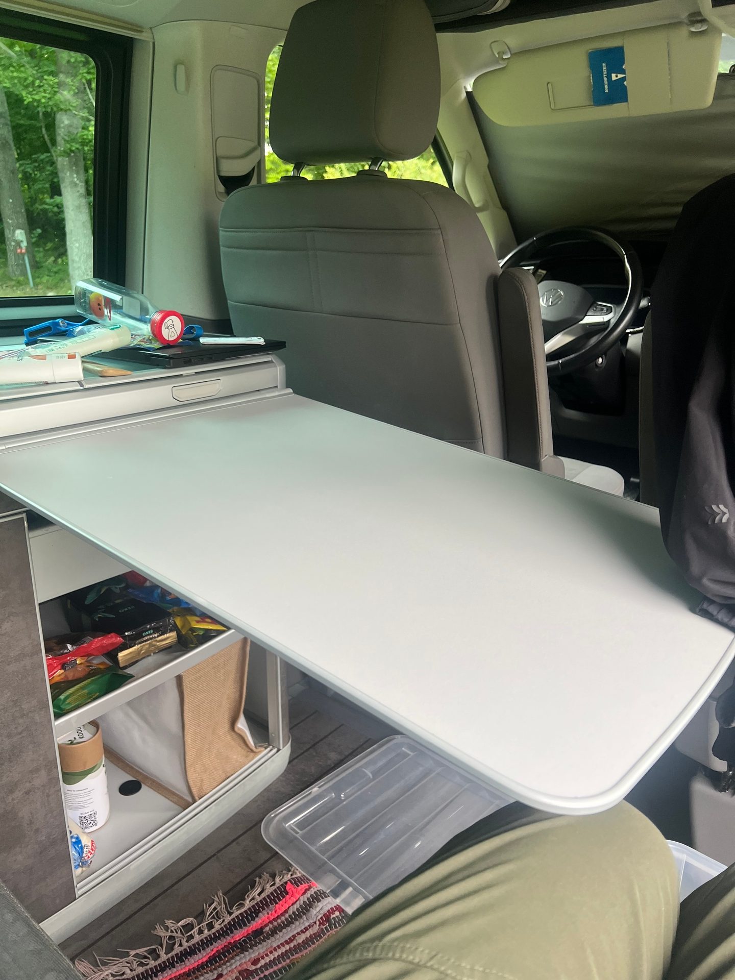 Camper van interior with an extended table, storage shelves, and driver's seat visible.