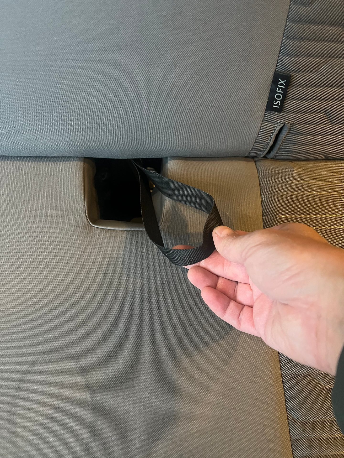 A hand pulls a black strap from a grey car seat, revealing an "ISOFIX" label.