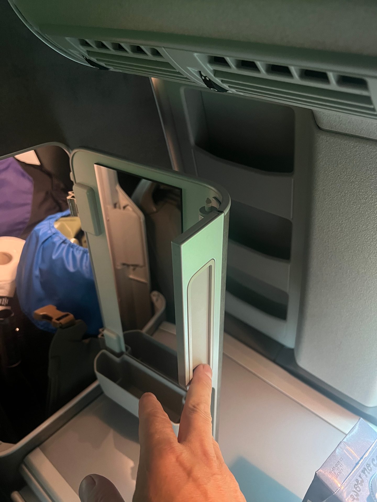 Hand opening a small refrigerator inside a vehicle, showing vents and storage.