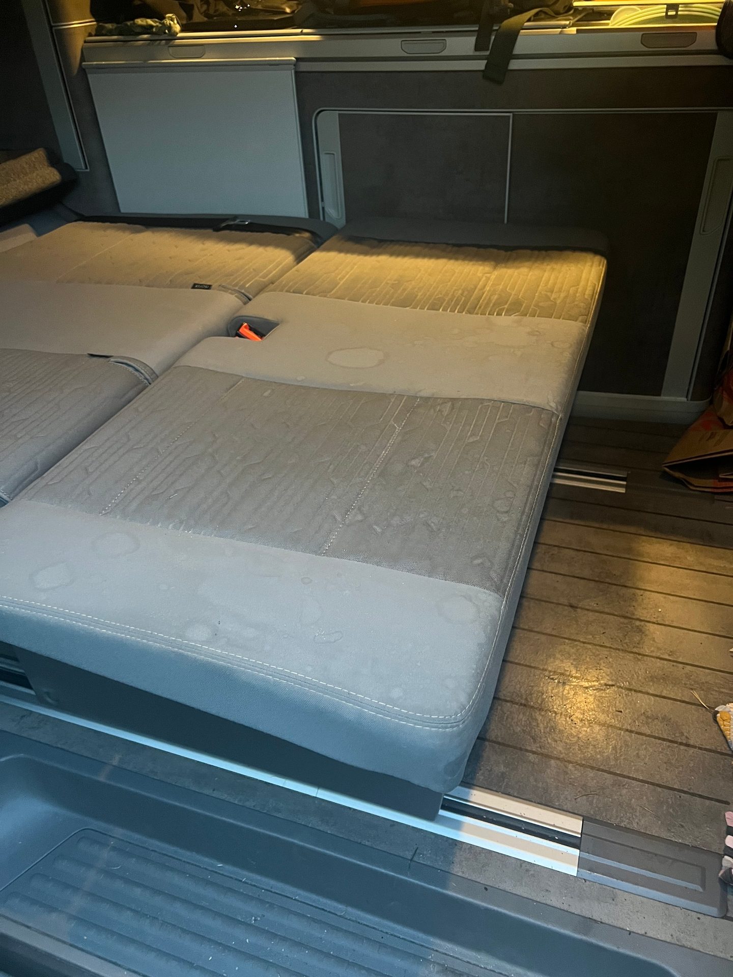 Camper van interior: grey seats folded into a bed, stained with water marks.