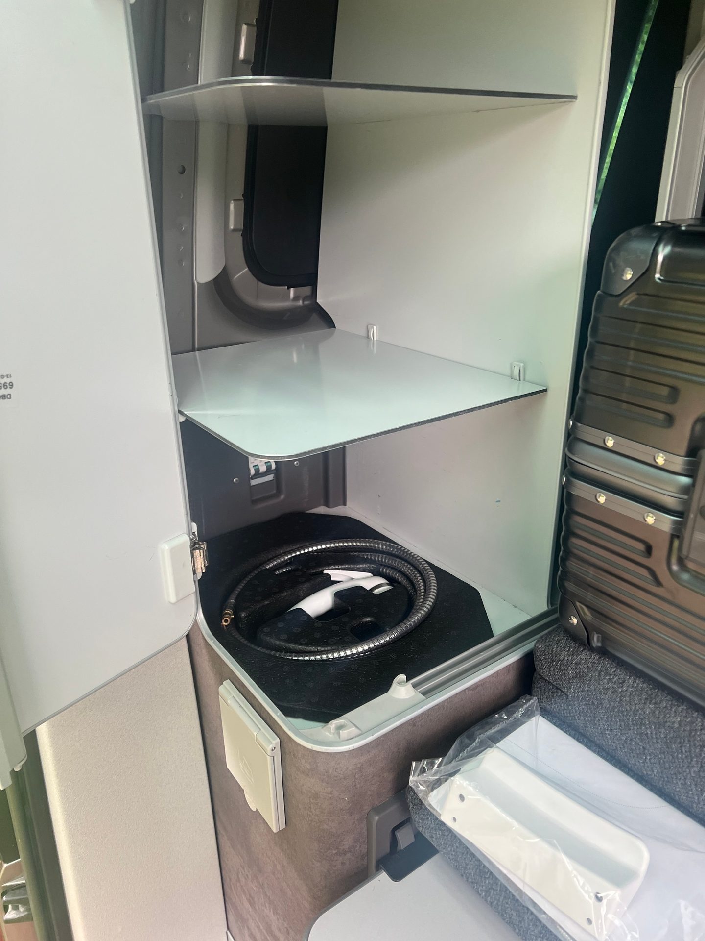 Open cabinet in a vehicle with shelves, a shower hose, and luggage.