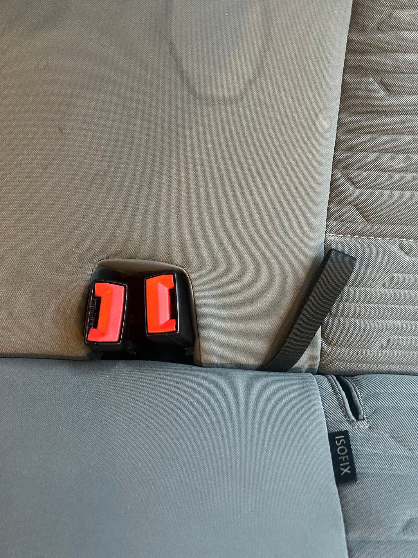 Stained car seat with a black and red seat belt buckle and an ISOFIX label.