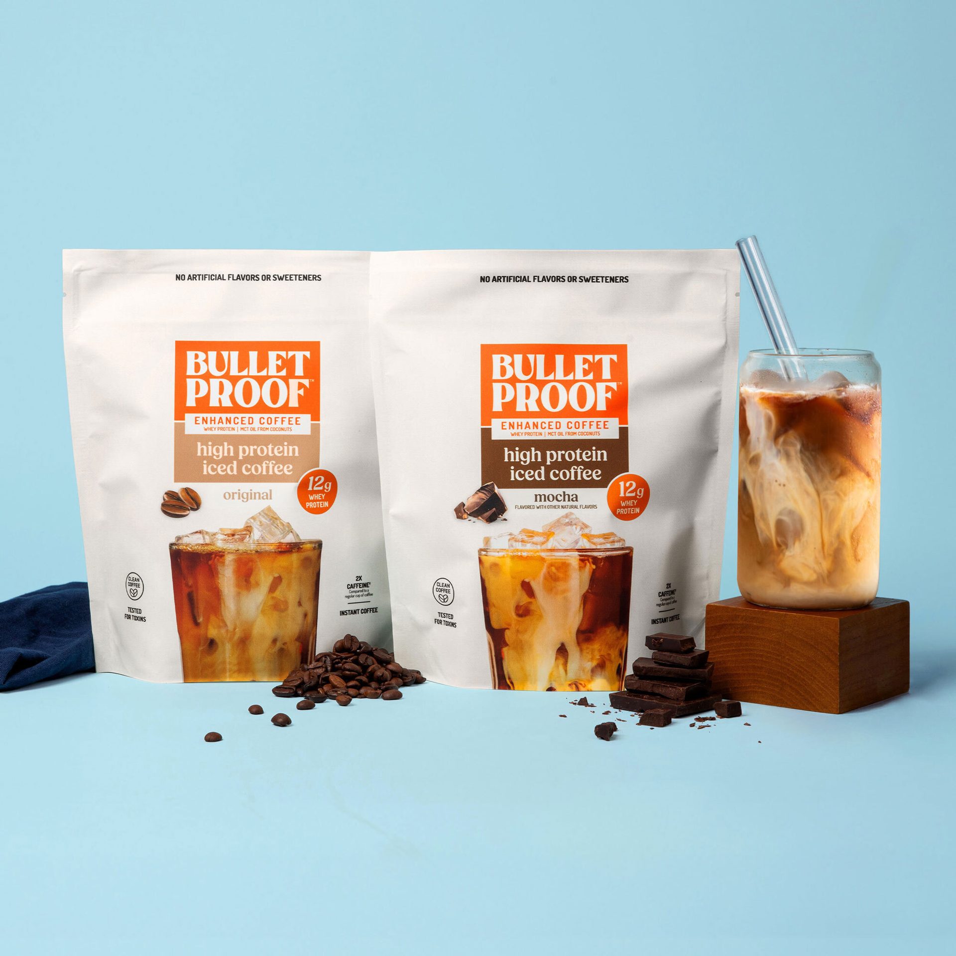 Two Bulletproof protein iced coffee bags (original, mocha), an iced coffee drink, beans, and chocolate.