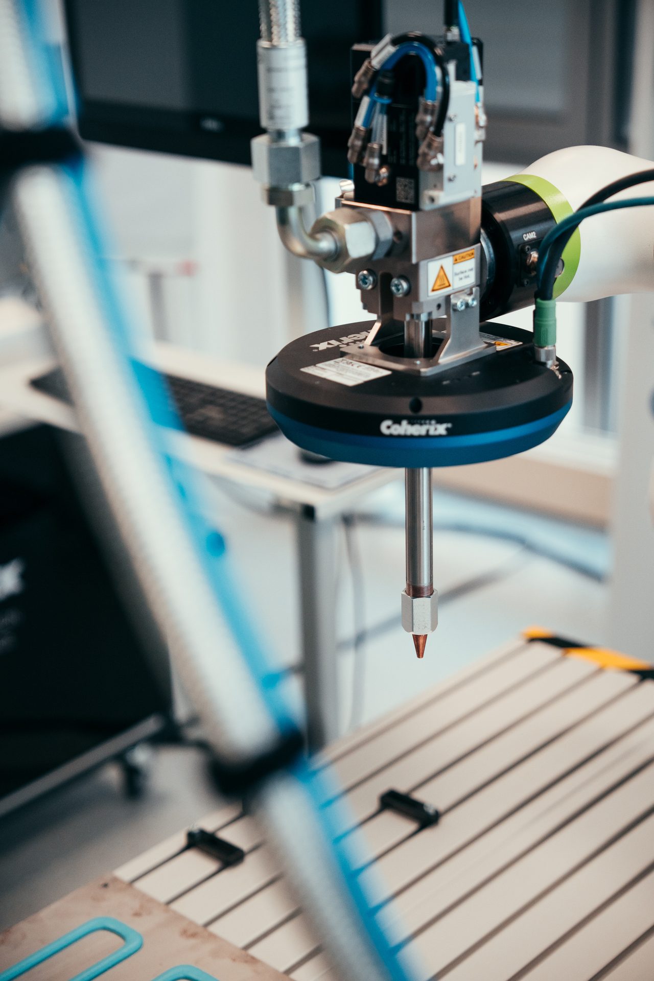 Robotic arm with a Coherix measurement sensor and pointed tip, poised over a patterned work surface.