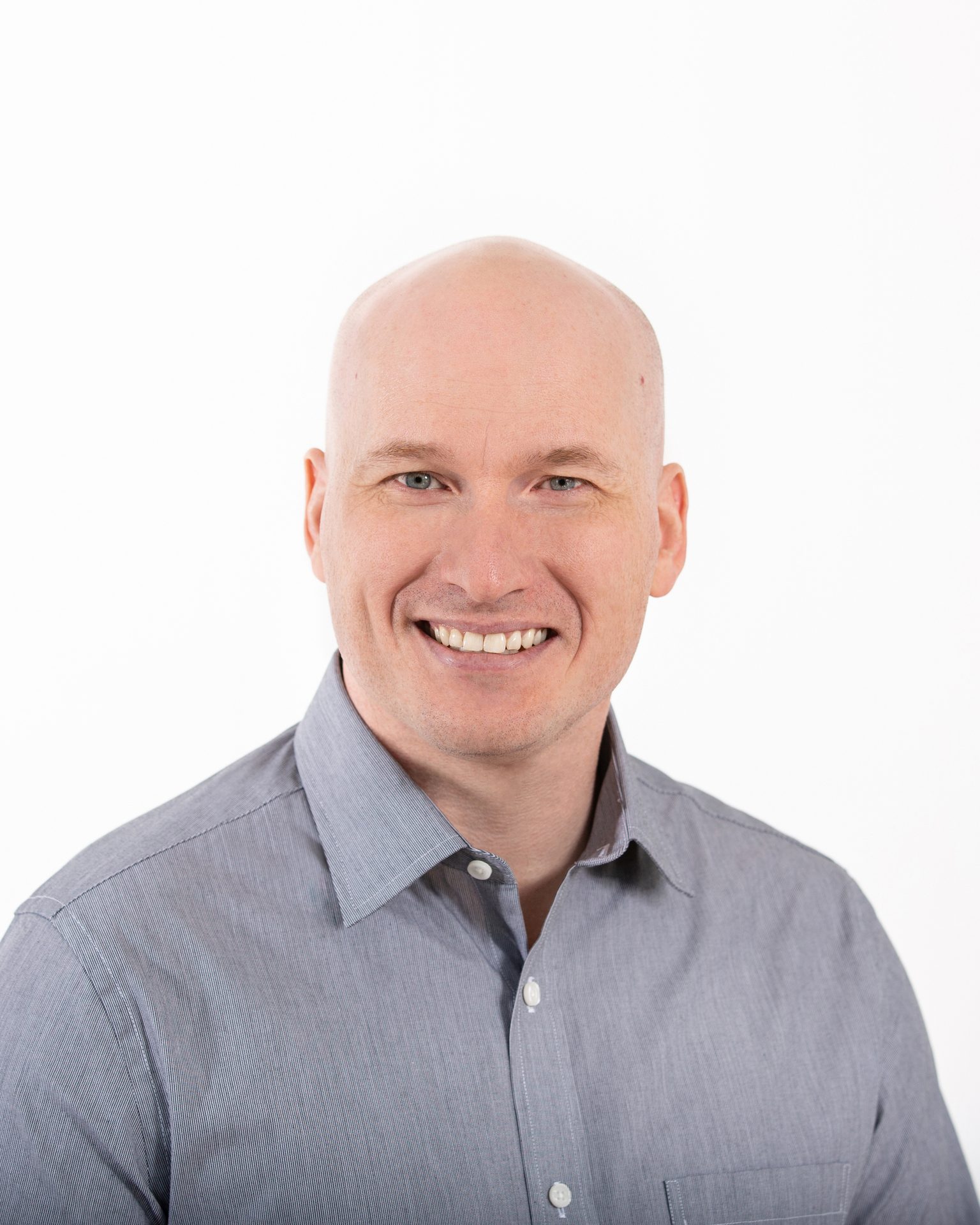 Smiling bald man in a gray shirt, looking at the camera.