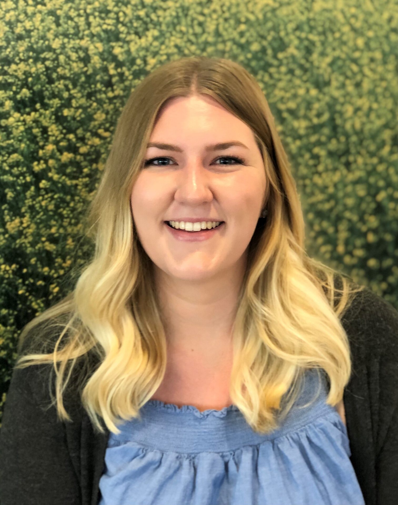 A smiling young woman with blonde hair in a blue top and grey cardigan.