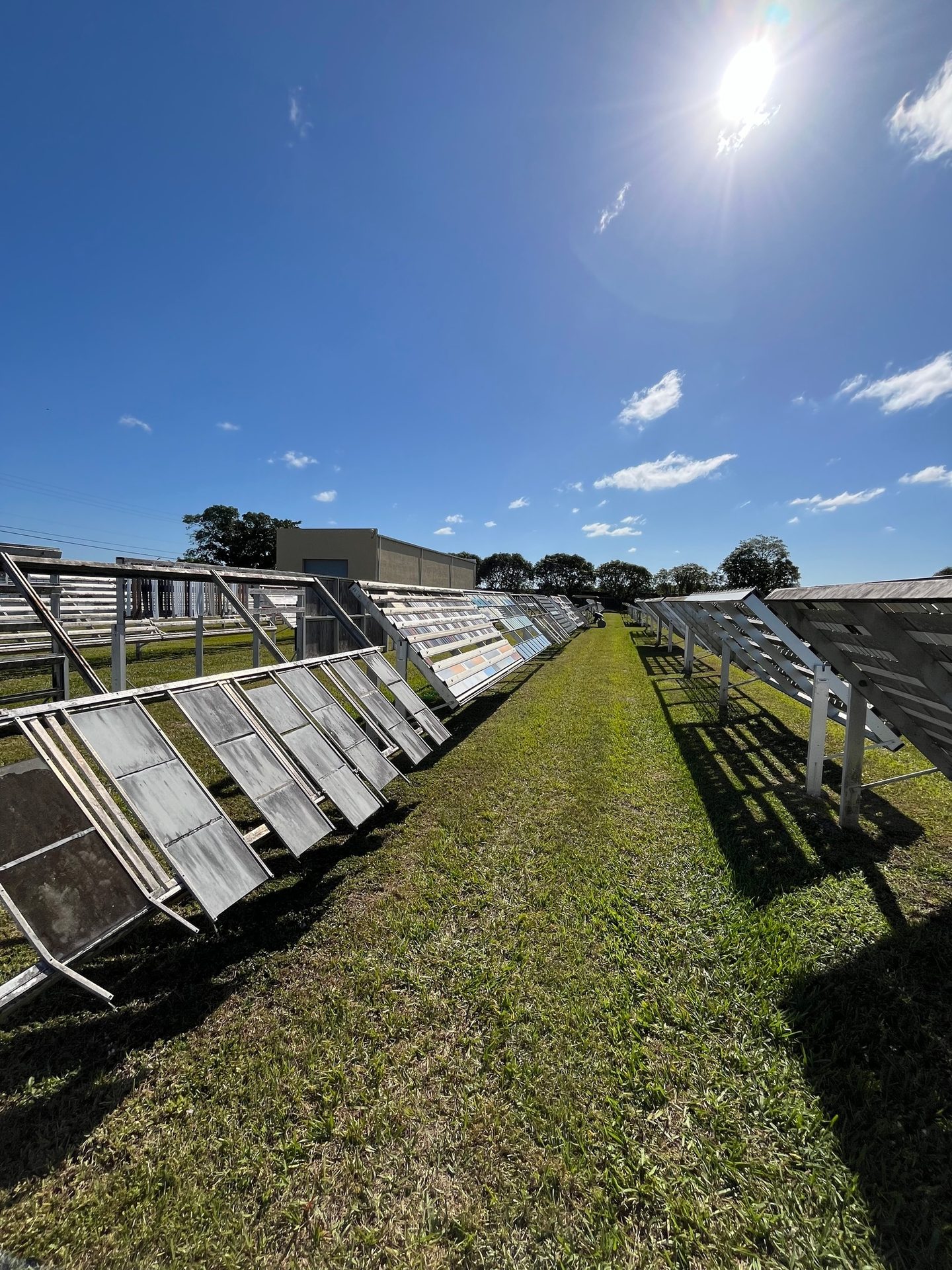 Rows of outdoor material testing racks on a sunny, grassy field under a blue sky.