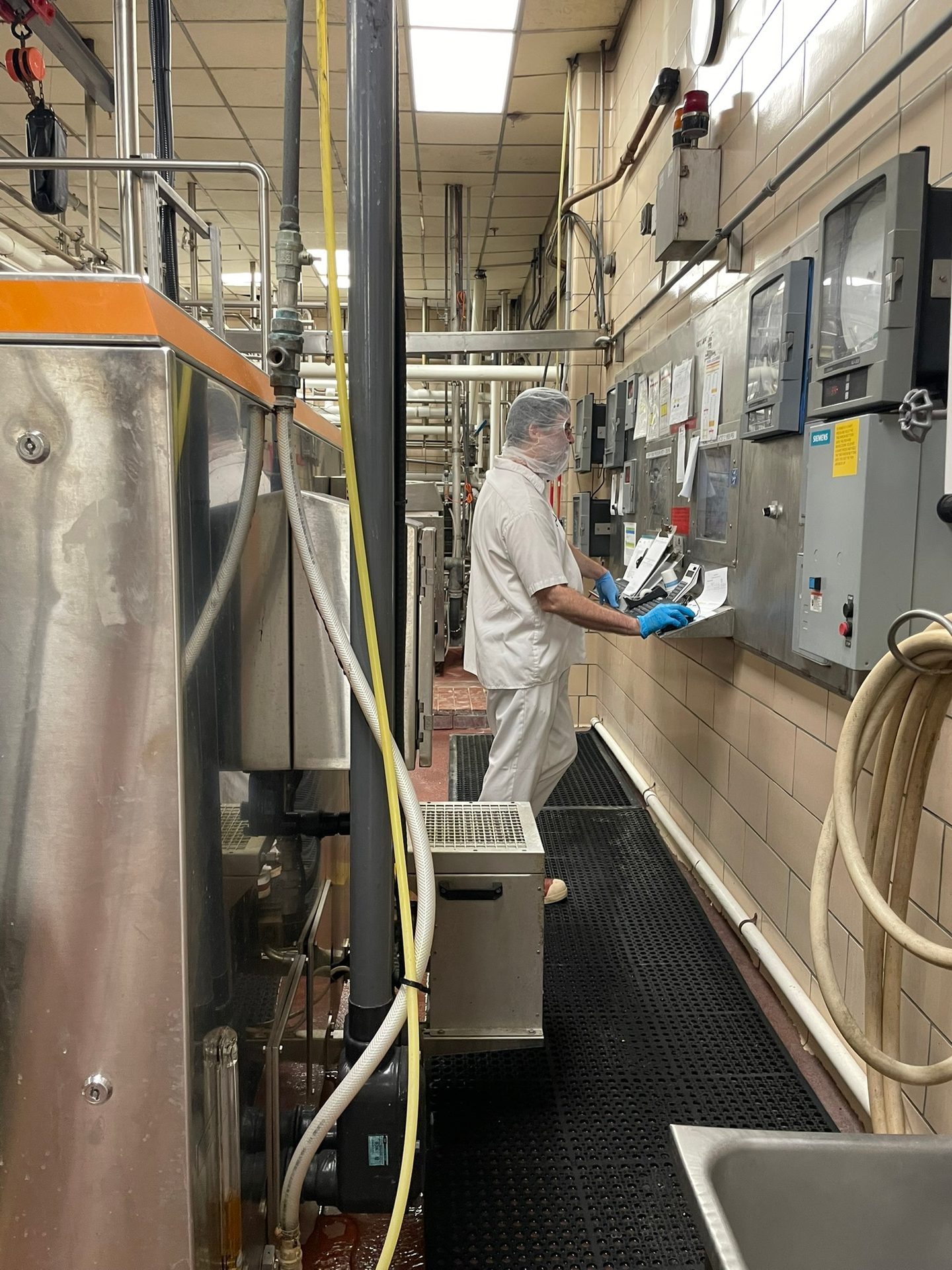 A worker in protective gear operates machinery and control panels in a busy industrial food processing plant.