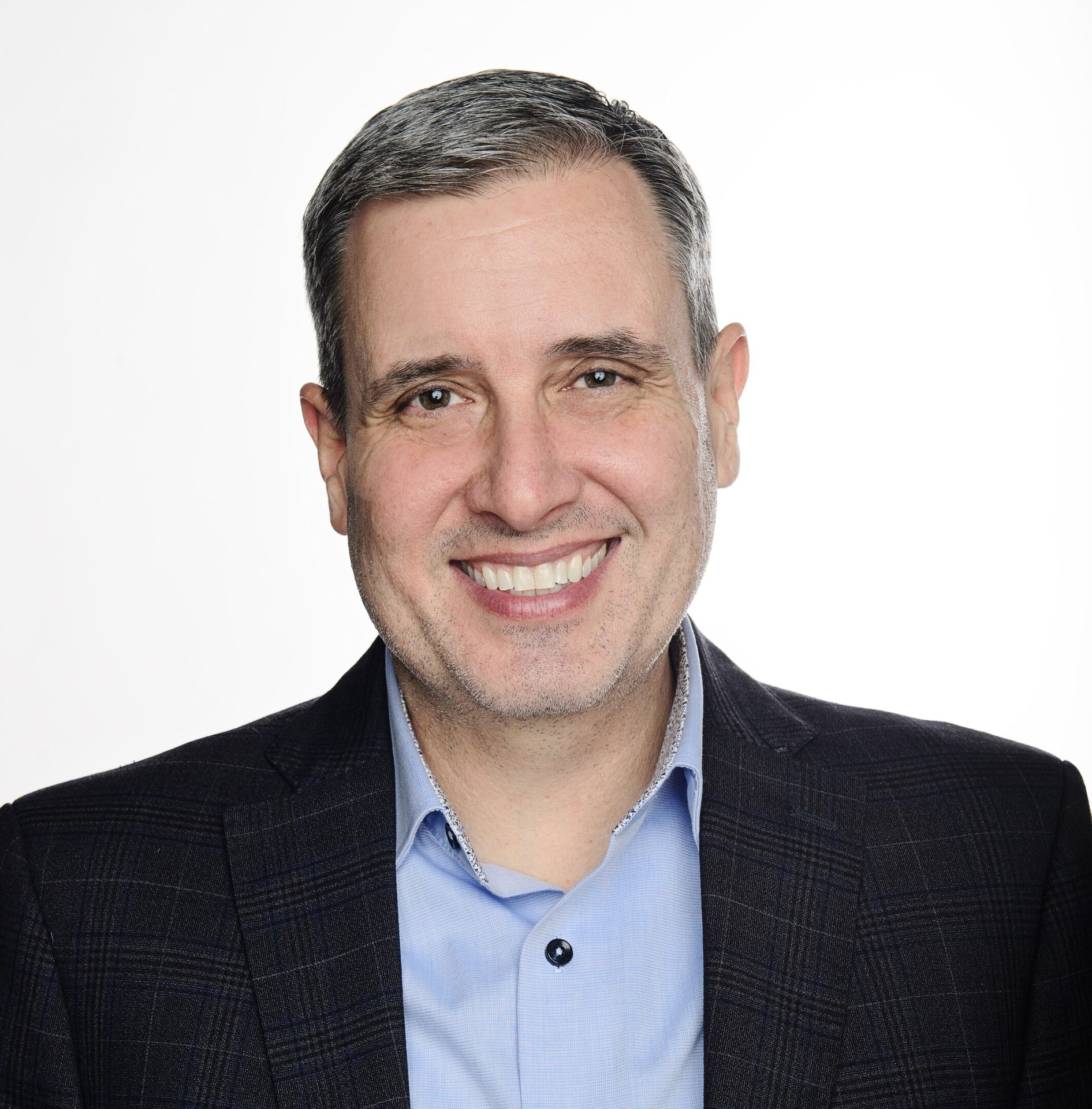 Portrait of a smiling man with grey hair in a blue shirt and dark suit jacket on white.