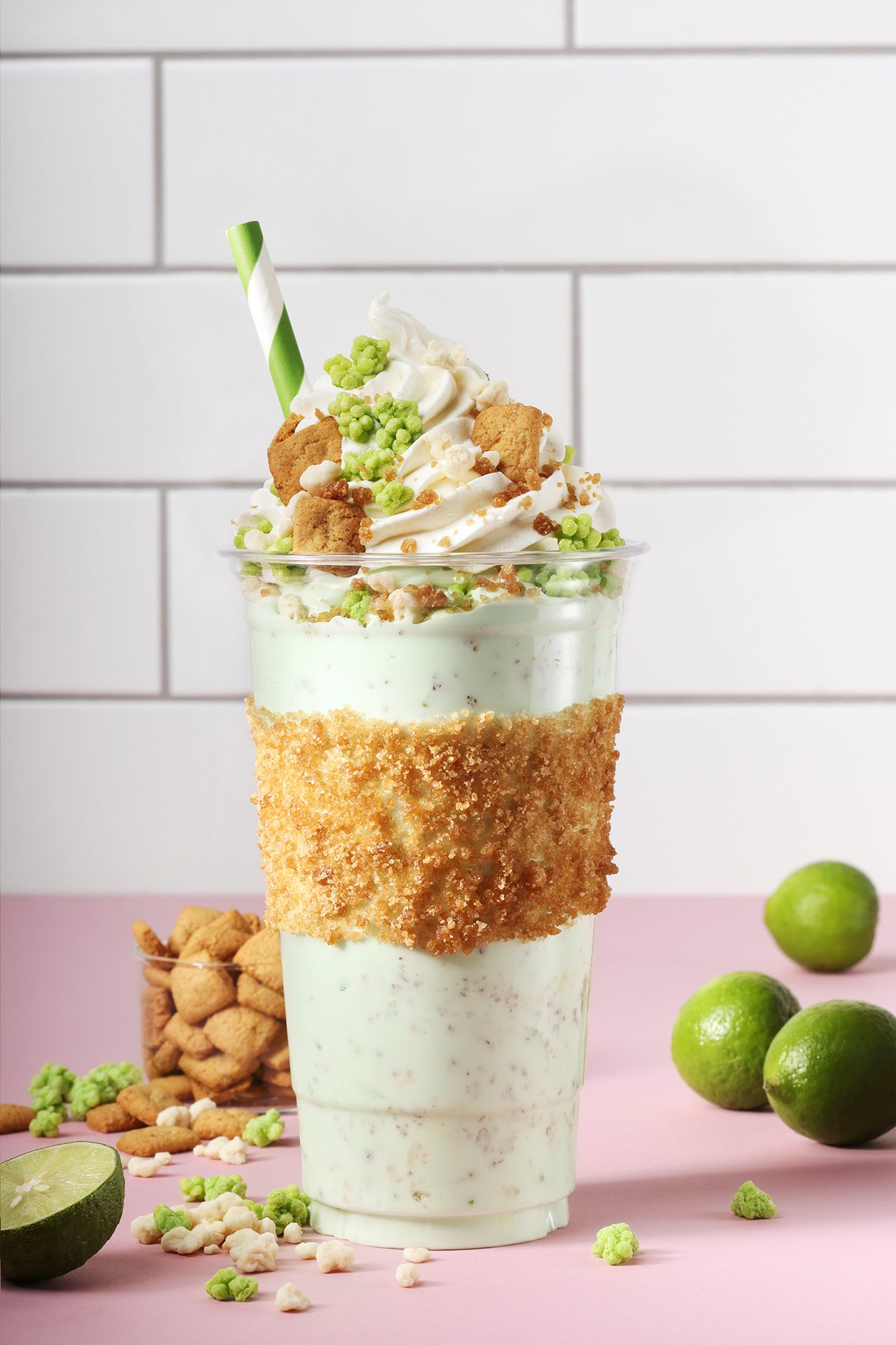 Key lime milkshake with whipped cream, cookies, and green sprinkles in a crusted cup, with limes.