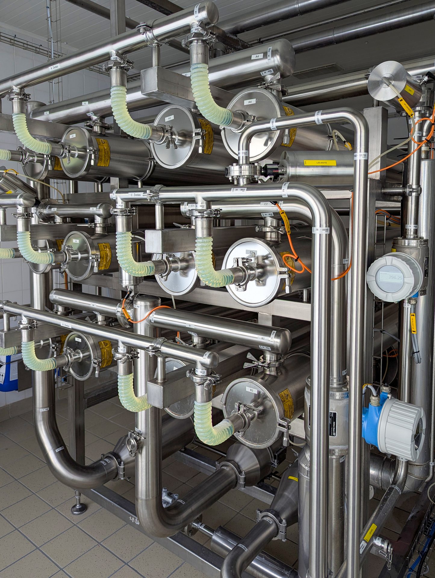 Industrial stainless steel piping, tanks, and filtration system with flexible hoses.