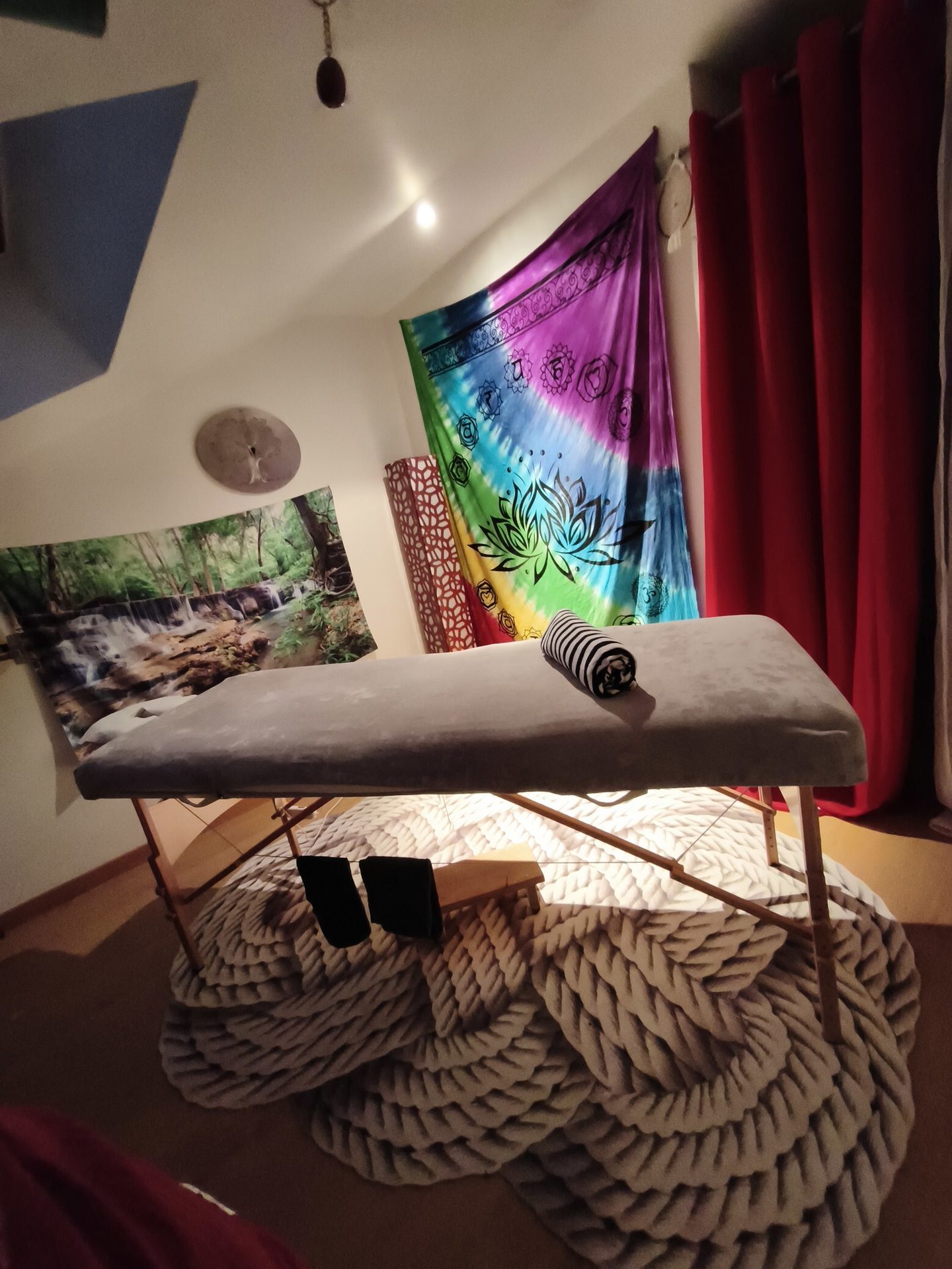 A cozy therapy room with a grey massage table, vibrant tapestries, and a large braided rug.